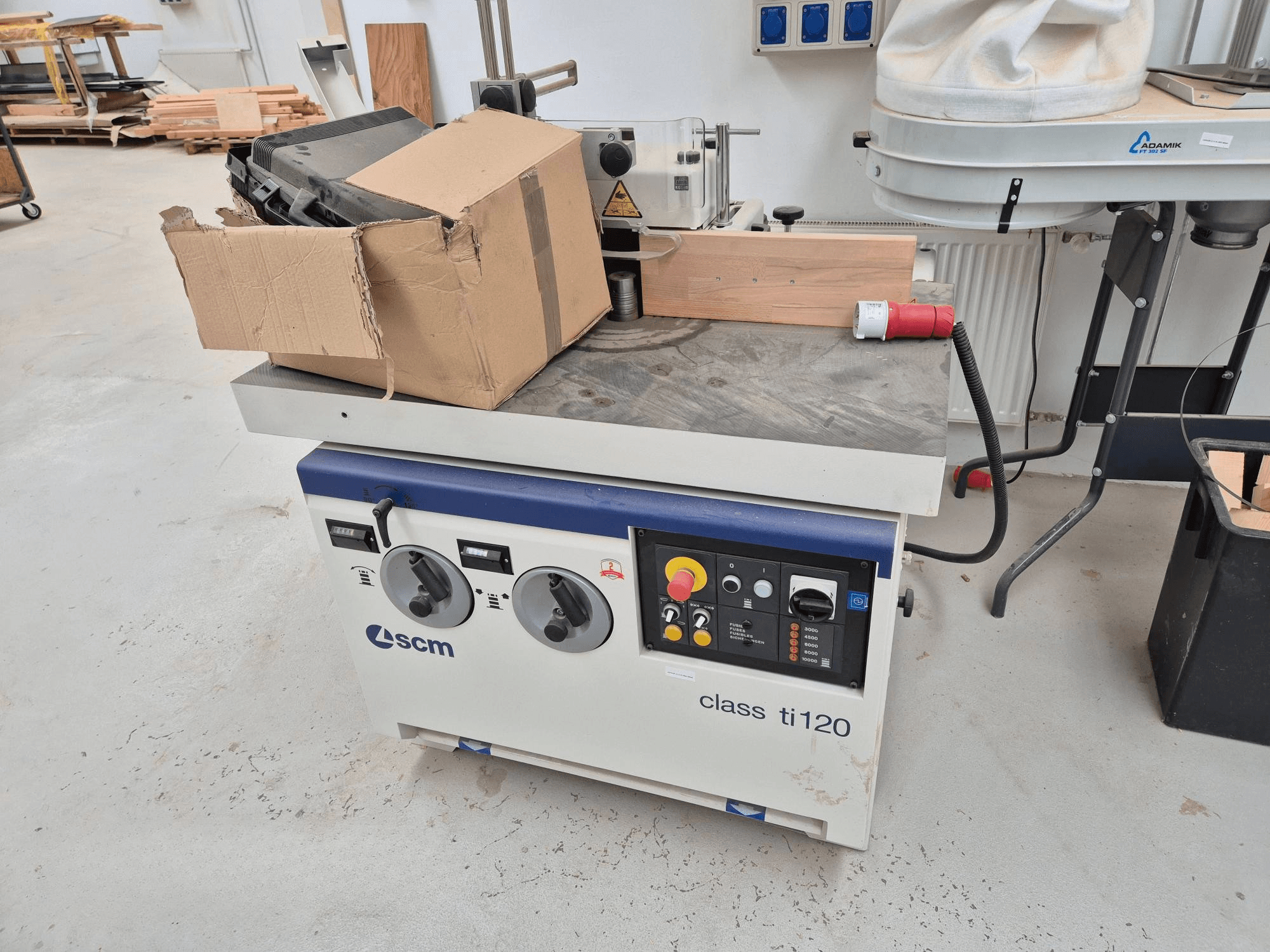 Máquina para trabajar la madera SCM clase ti120, vista frontal, presenta un panel de control con mandos y botones, además de una caja de cartón adjunta.