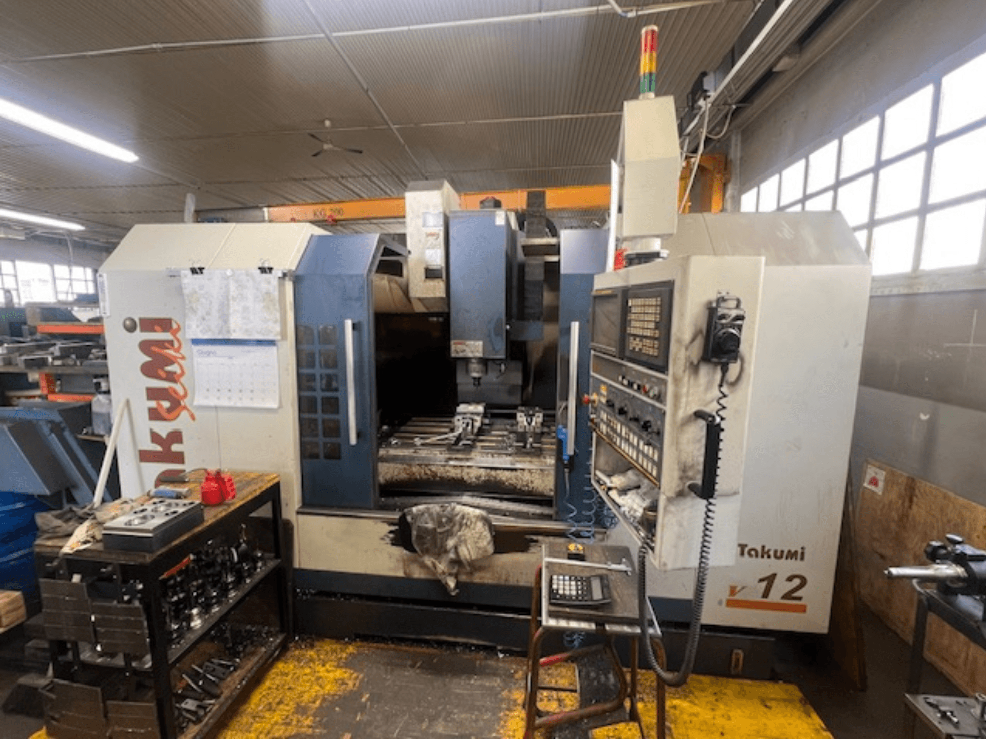 Fresadora CNC Takumi V12 en vista lateral, mostrando el panel de control, el área de corte y las herramientas en la estación de trabajo.