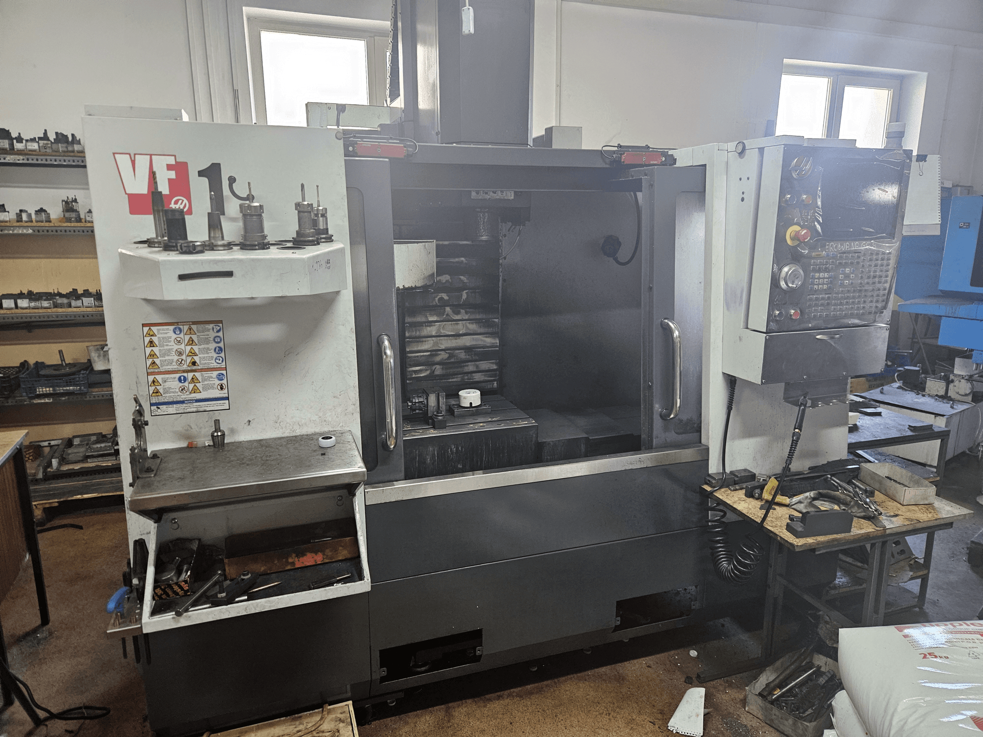 Centro de mecanizado vertical HAAS VF-1, vista frontal con herramientas en el lateral, panel de control visible y espacio de trabajo al fondo.