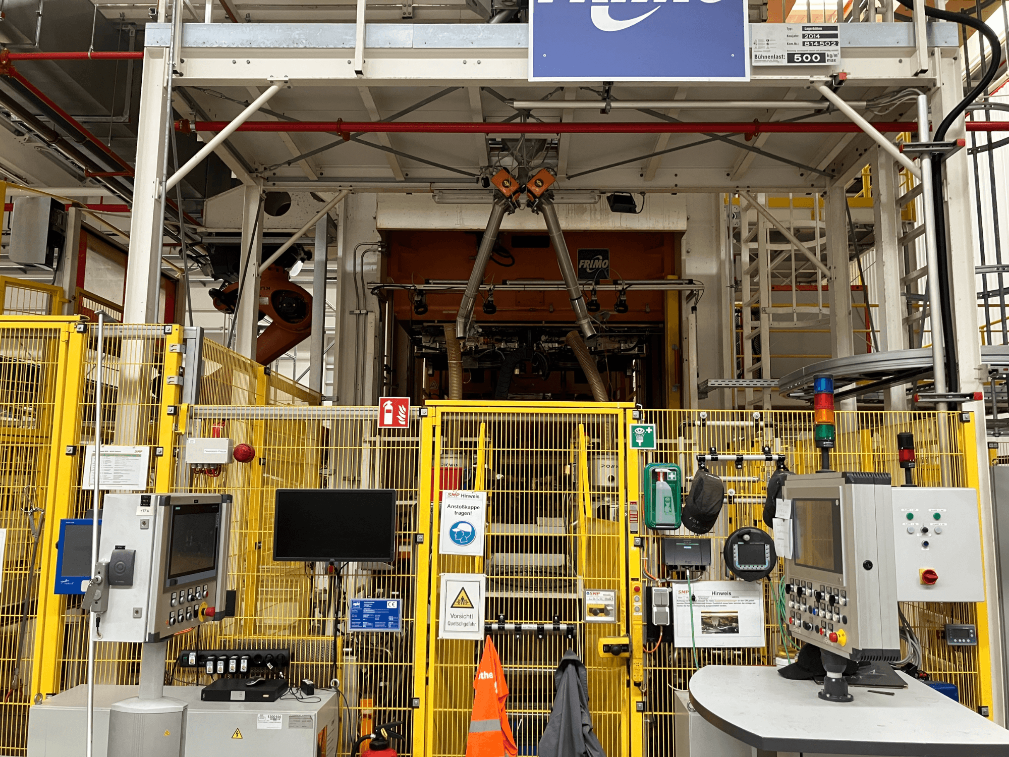 Vista frontal de la planta de termoformado FRIMO NFPP, con paneles de control y vallas de seguridad en un entorno industrial bien iluminado.