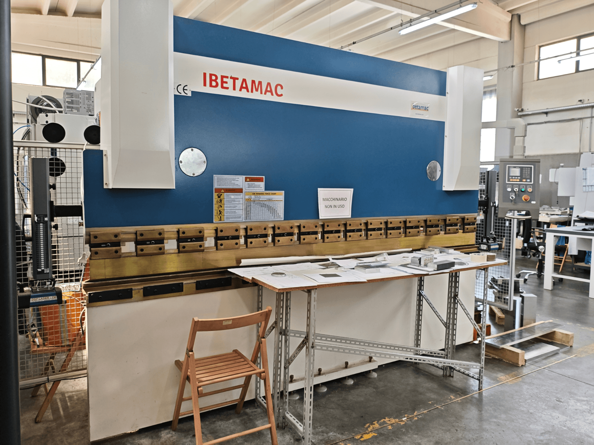 Plegadora IBETAMAC 3200 100T en un taller; vista lateral en la que se aprecian el panel de control, la zona de trabajo y las indicaciones de seguridad.