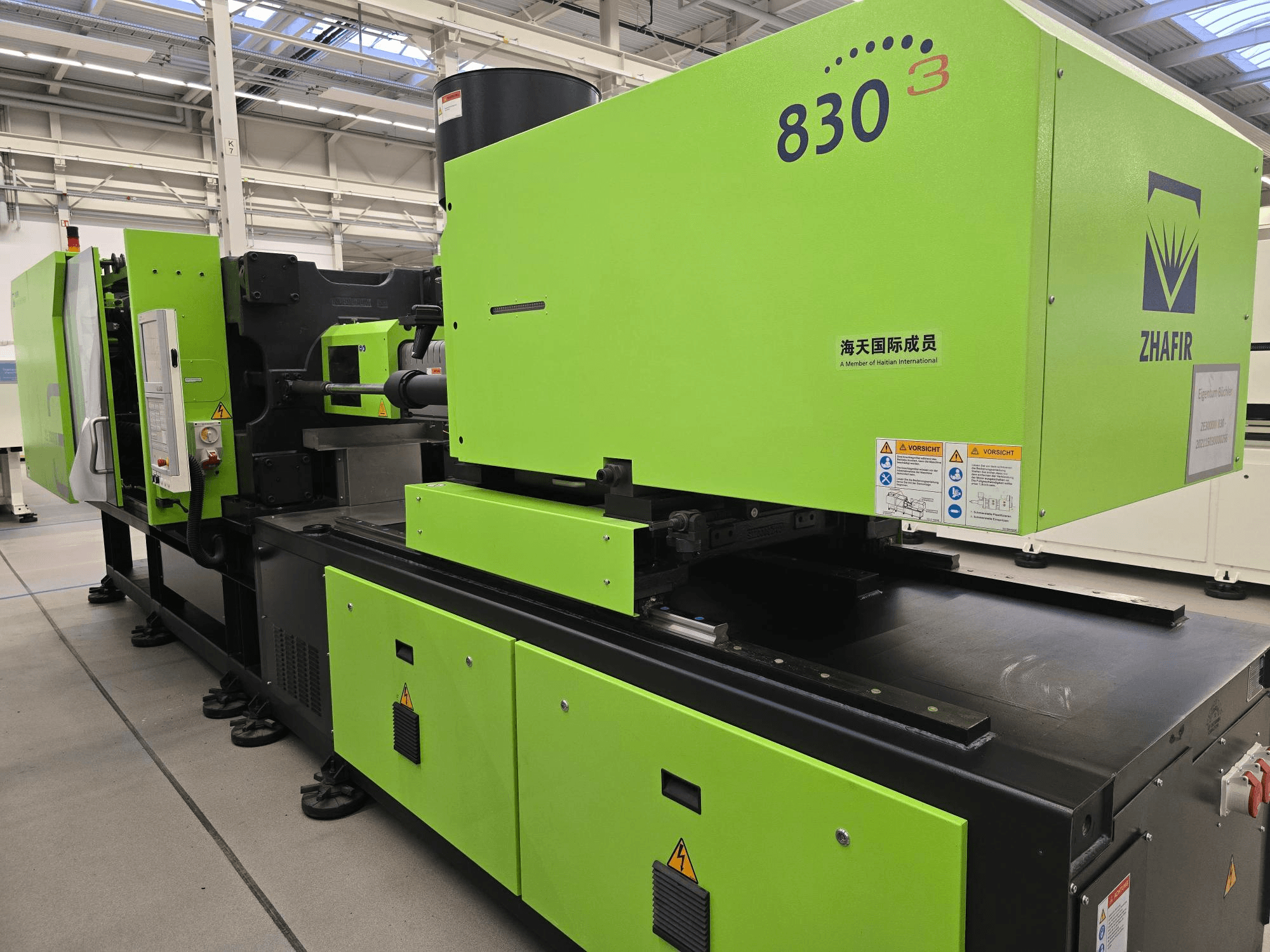 Máquina de moldeo por inyección eléctrica ZHAFIR ZERES III 3000/830/B5, vista lateral, con la carcasa verde brillante y el panel de control visibles.