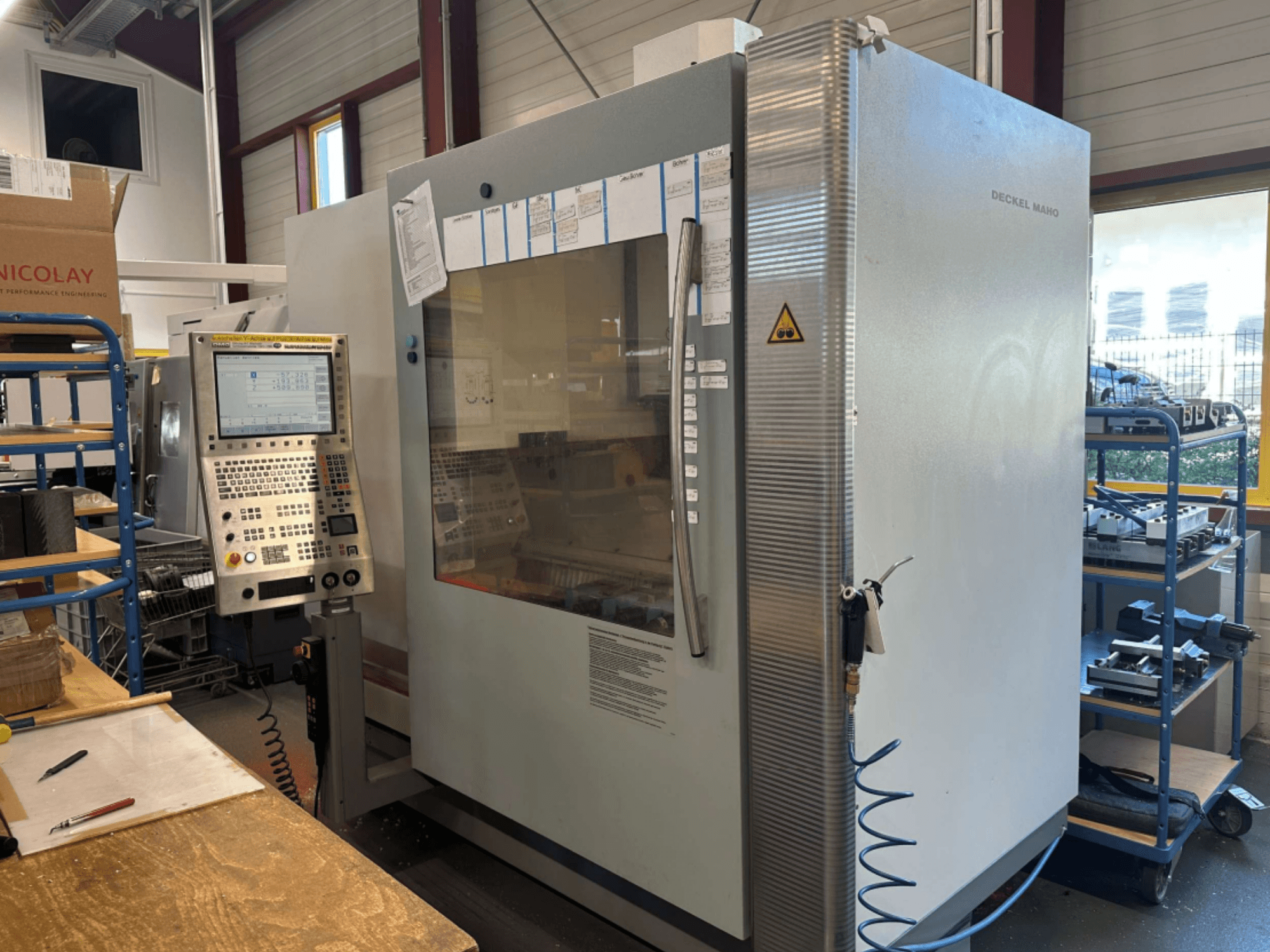 Centro de mecanizado vertical DMG DECKEL MAHO 1035V, vista lateral mostrando el panel de control y la estructura de la máquina, en un entorno de taller.