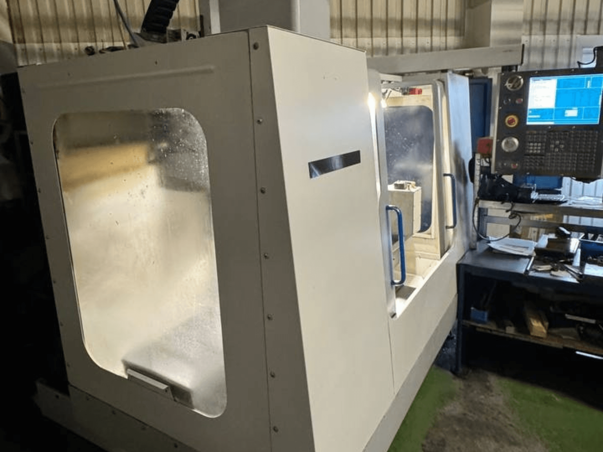 Centro de mecanizado vertical HAAS VCE 750 en vista lateral, con panel de control y carcasa de seguridad transparente.