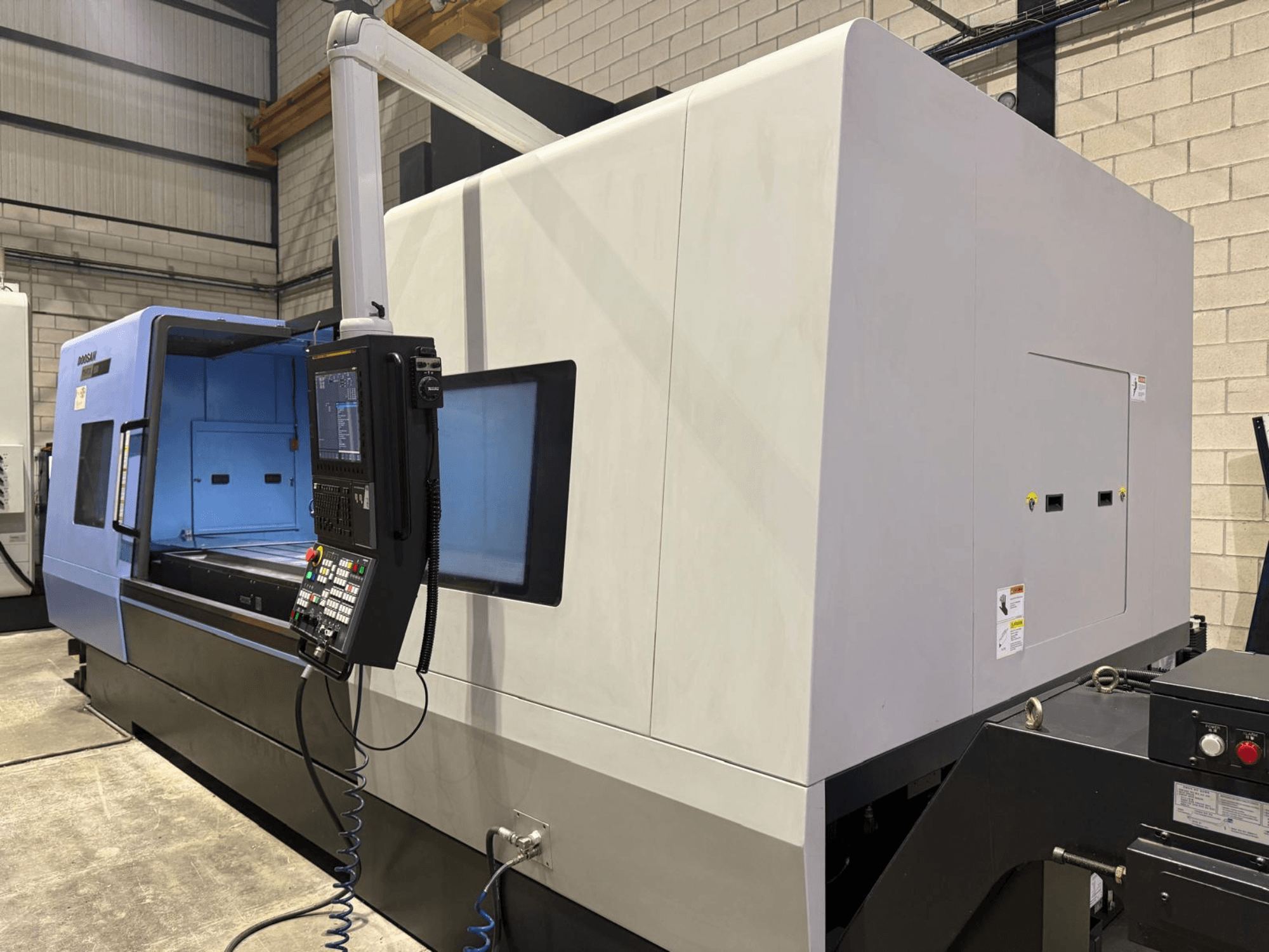 Torno CNC industrial, exterior azul y gris, vista frontal; dispone de panel de control con botones y pantalla para operaciones precisas.