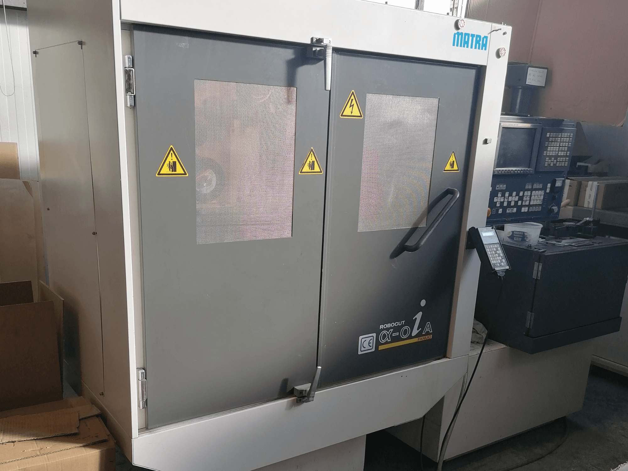 Máquina Robocut α-oZα de Matra, vista frontal que muestra las advertencias de seguridad, el panel de control y las puertas dobles con ventanas de malla.