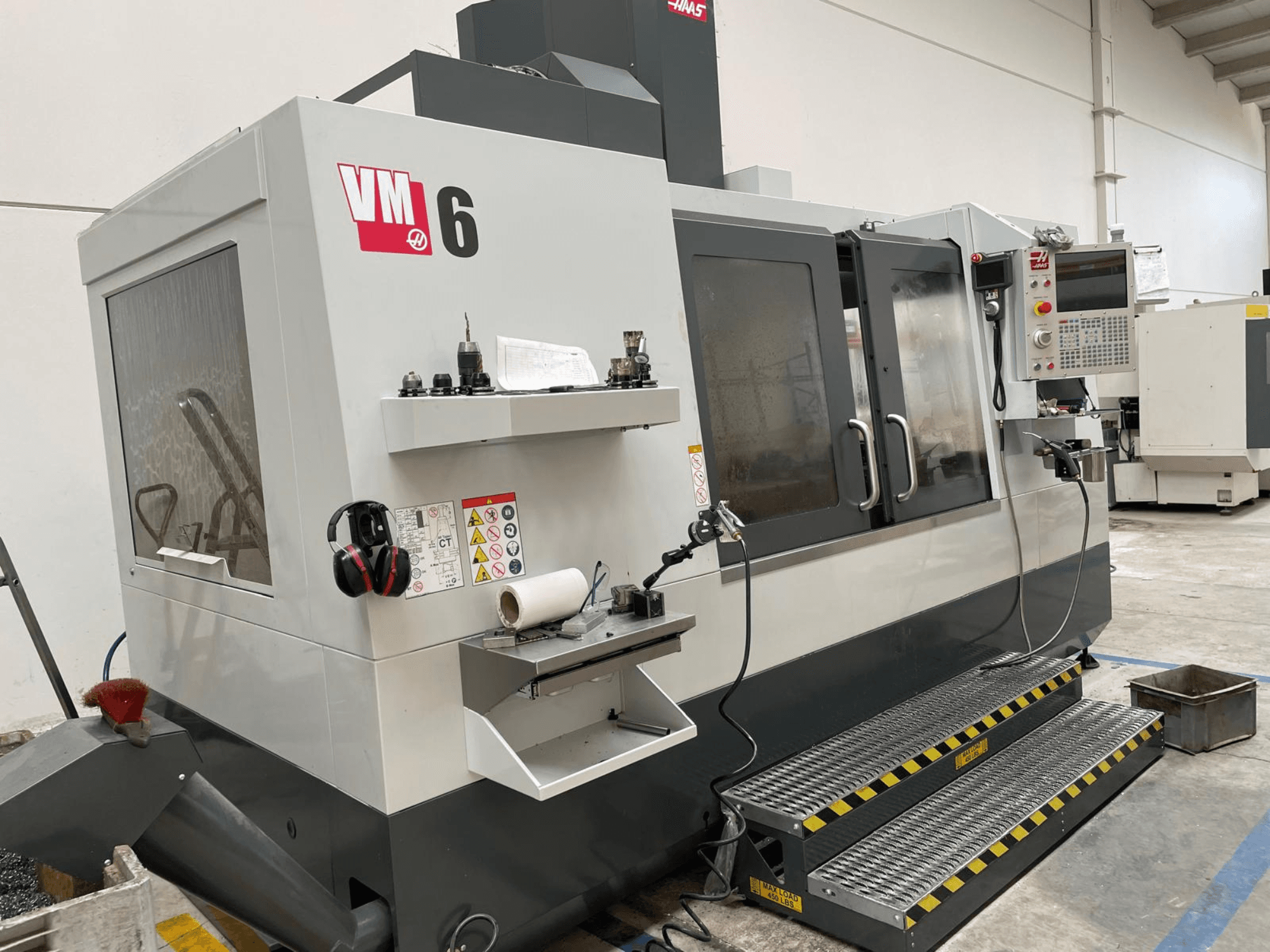 Centro de mecanizado vertical Haas VM-6, vista frontal que muestra el panel de control, los portaherramientas y los dispositivos de seguridad.