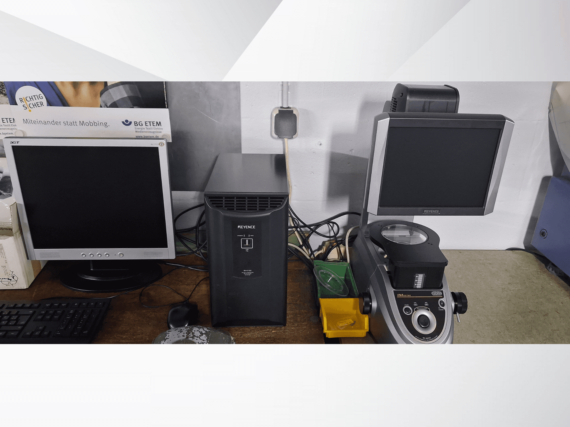 Dos monitores de ordenador, uno Acer y otro Keyence, junto a un dispositivo negro y un microscopio, vistos de frente.