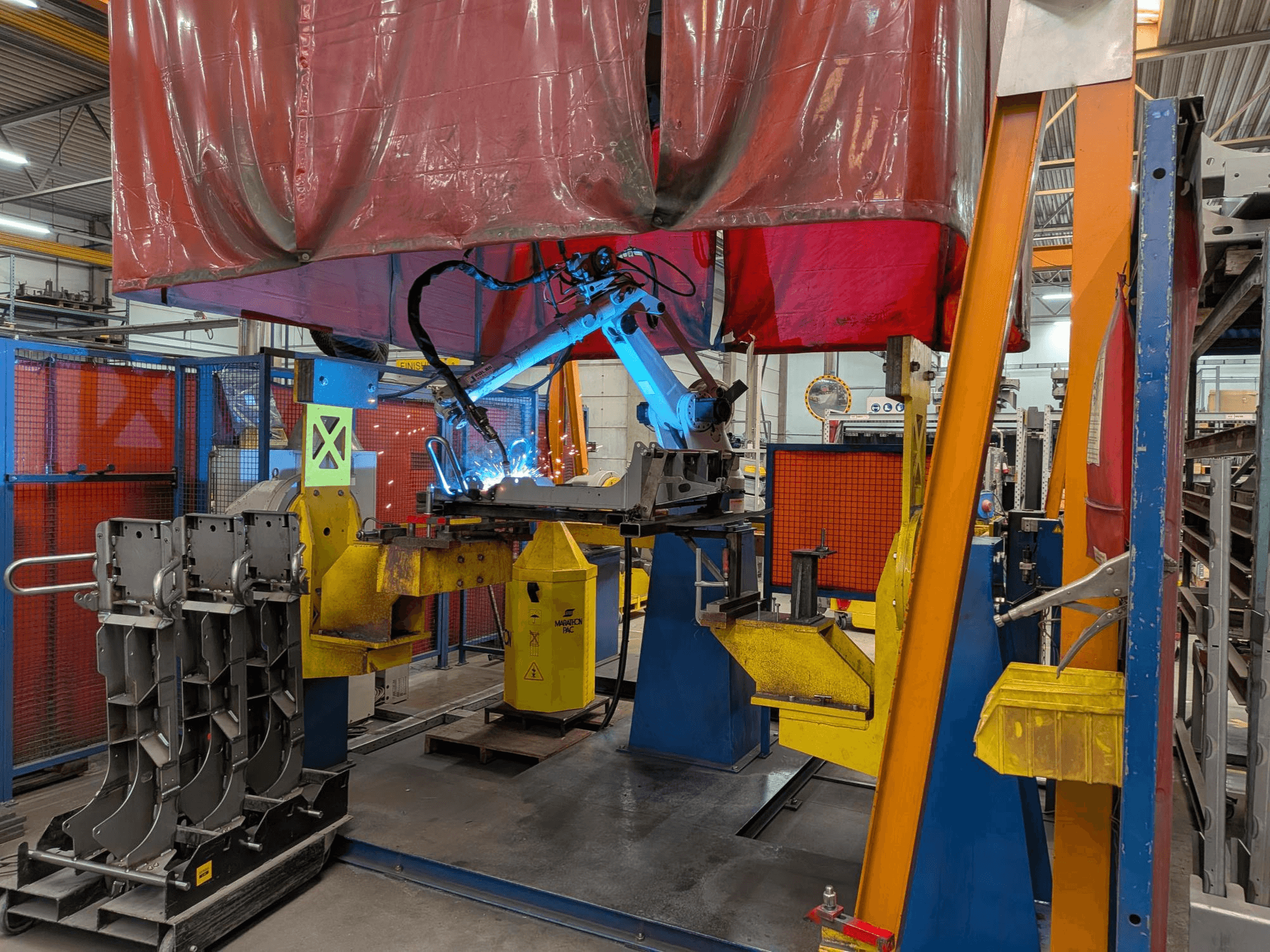 El robot de soldadura OTC Daihen DR4200 en acción, visto desde delante, con un arco de soldadura de color azul brillante y una cubierta protectora.