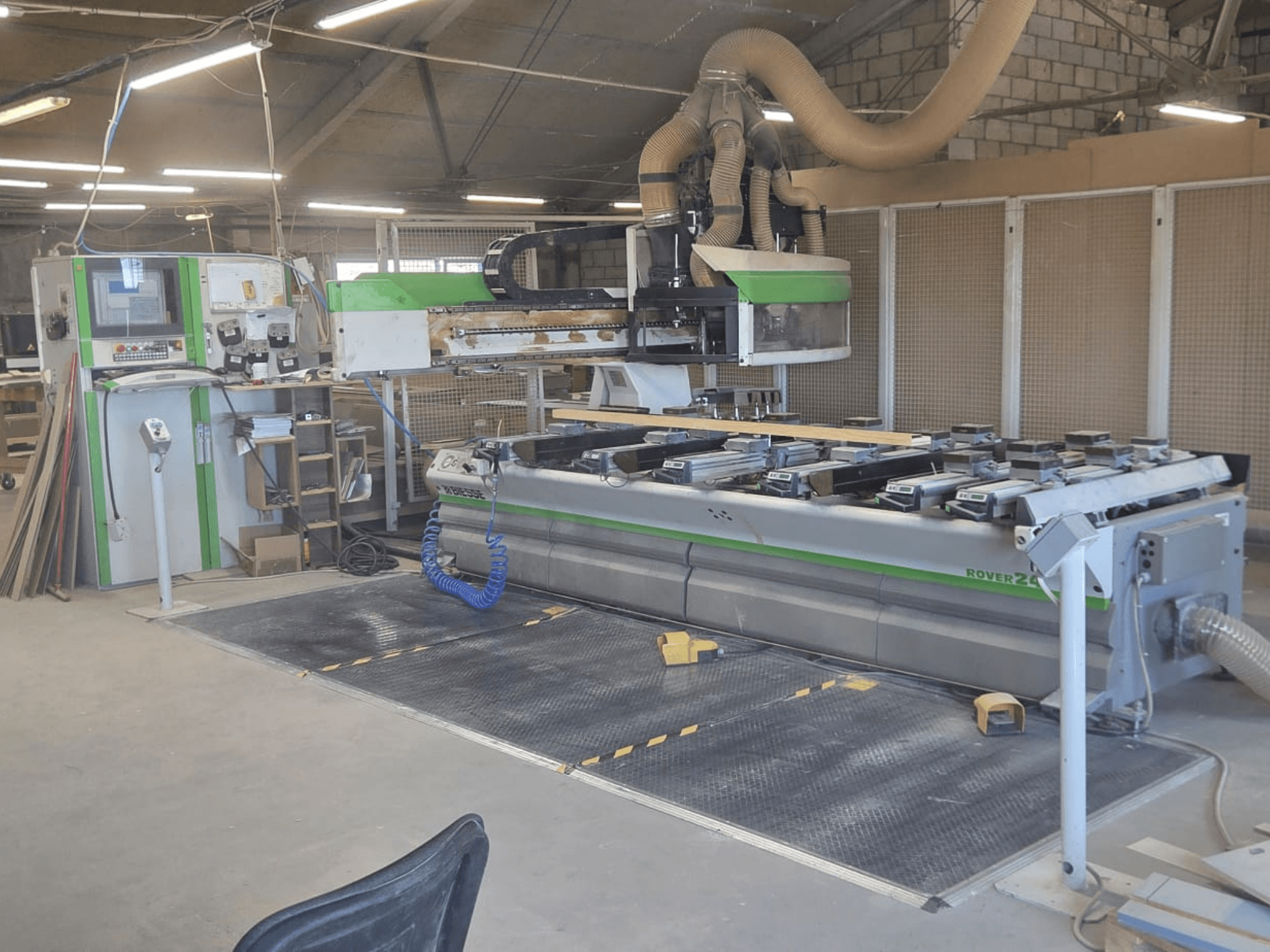 Centro de mecanizado CNC BIESSE Rover 24S en un taller, con panel de control y gran superficie de trabajo con piezas de madera.