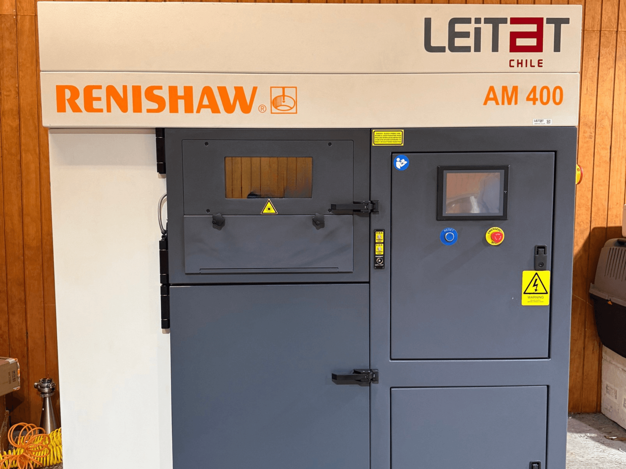 Vista frontal de la impresora 3D de metal RENISHAW AM400, en la que se aprecian el panel de control, las etiquetas de advertencia y el acceso para el mantenimiento.