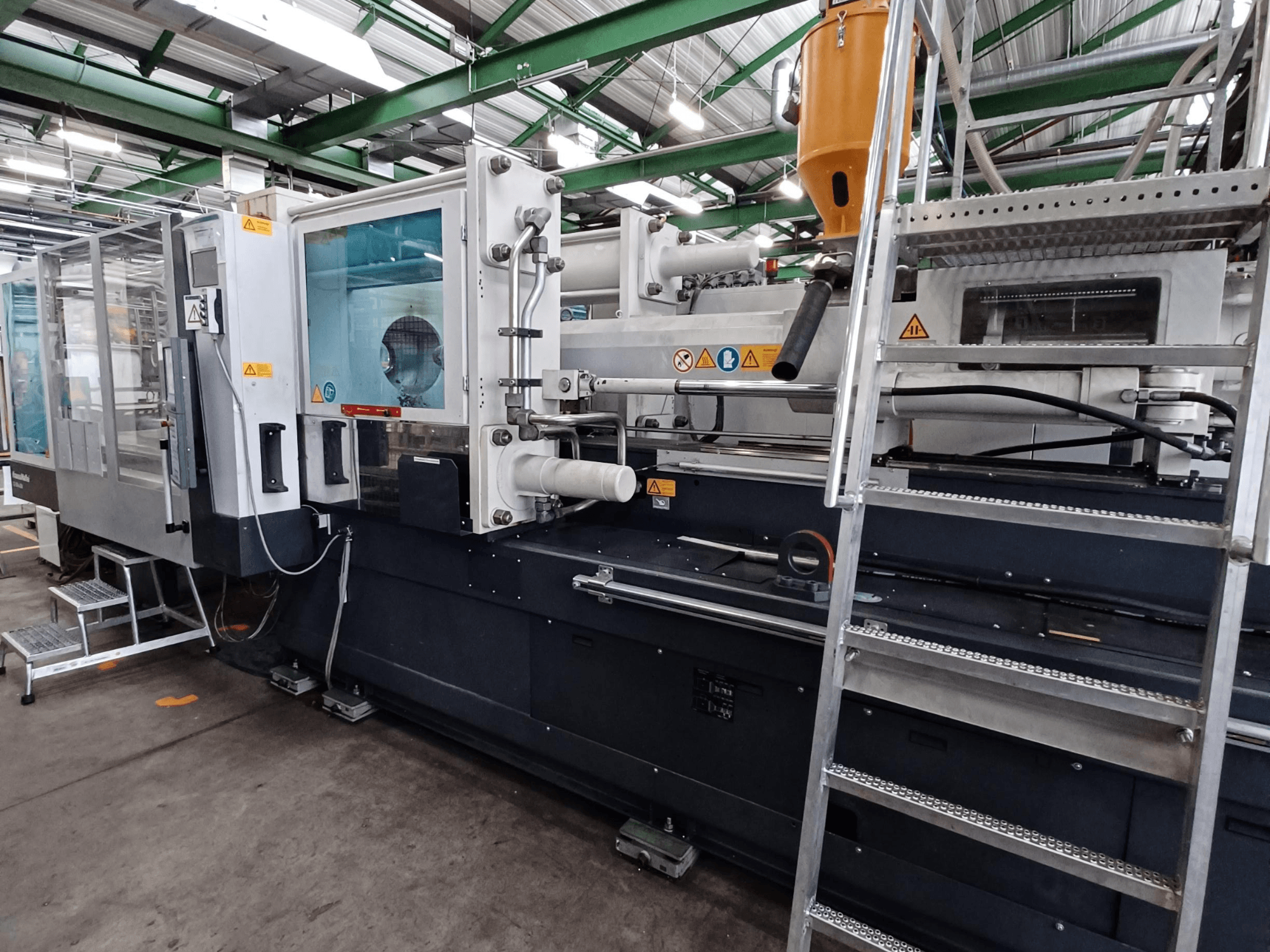 Máquina de moldeo por inyección industrial con una vista frontal clara, que muestra las marcas, el panel de control y la tolva de material.