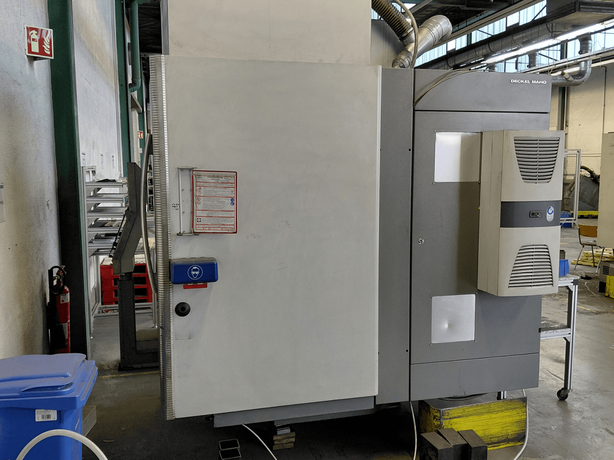 Vista lateral del centro de mecanizado vertical DECKEL MAHO DMC 635 V con el panel de control y las etiquetas de seguridad visibles.