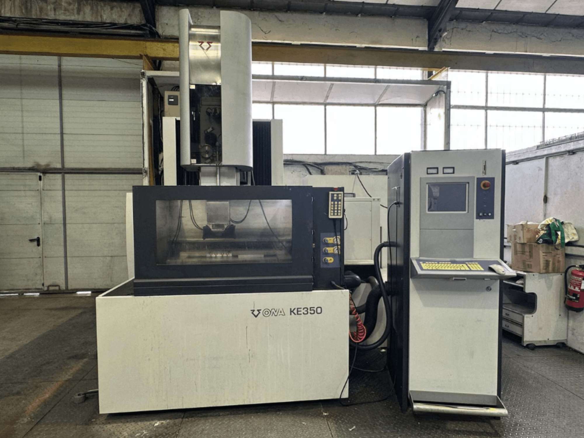 Vista frontal de la máquina CNC ONA KE350 con panel de control, pantalla de visualización y varios botones, situada en un entorno industrial.