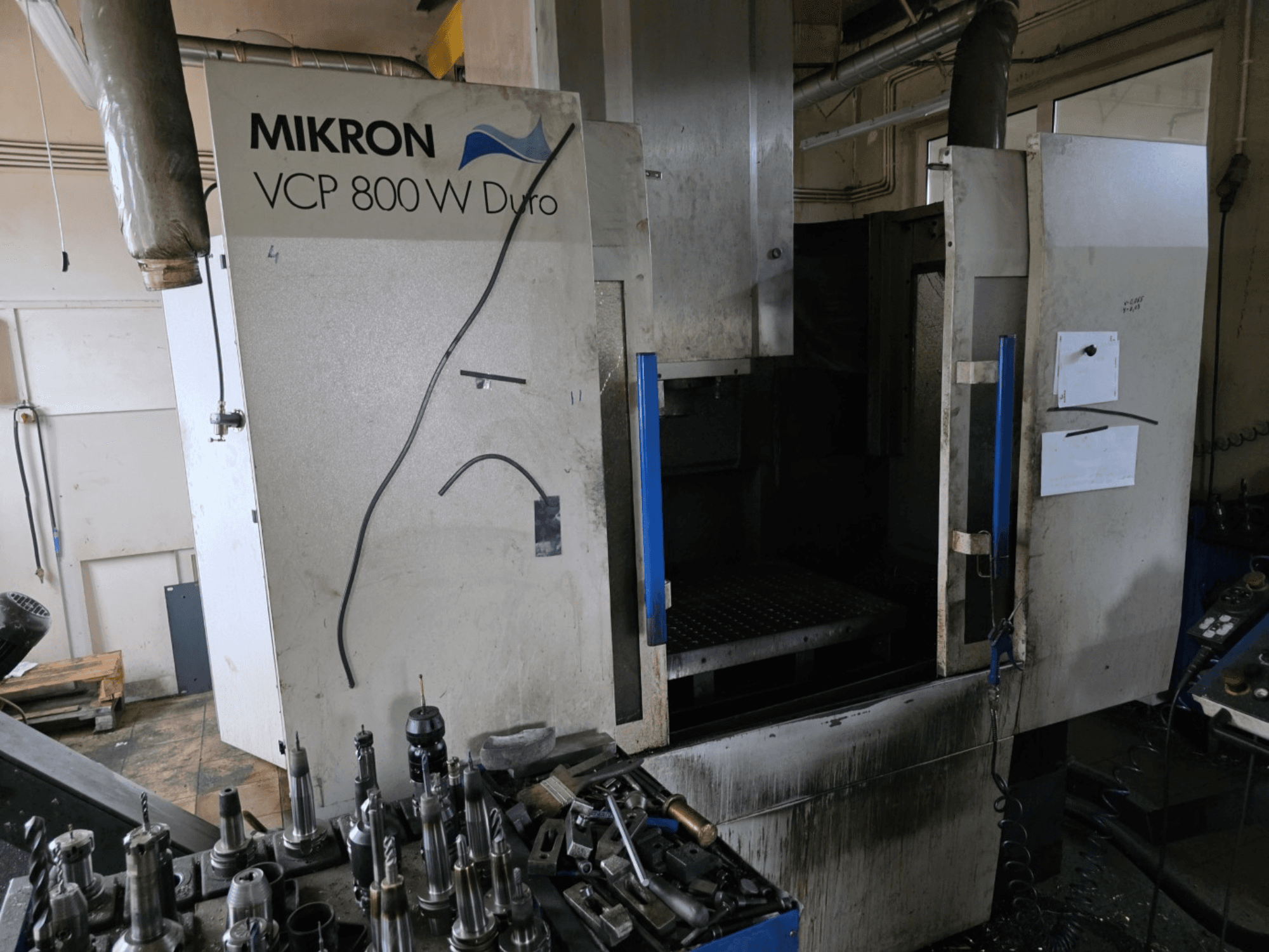 Fresadora Mikron VCP 800 W Duro mostrada desde una vista lateral, con las herramientas y los controles visibles en primer plano.