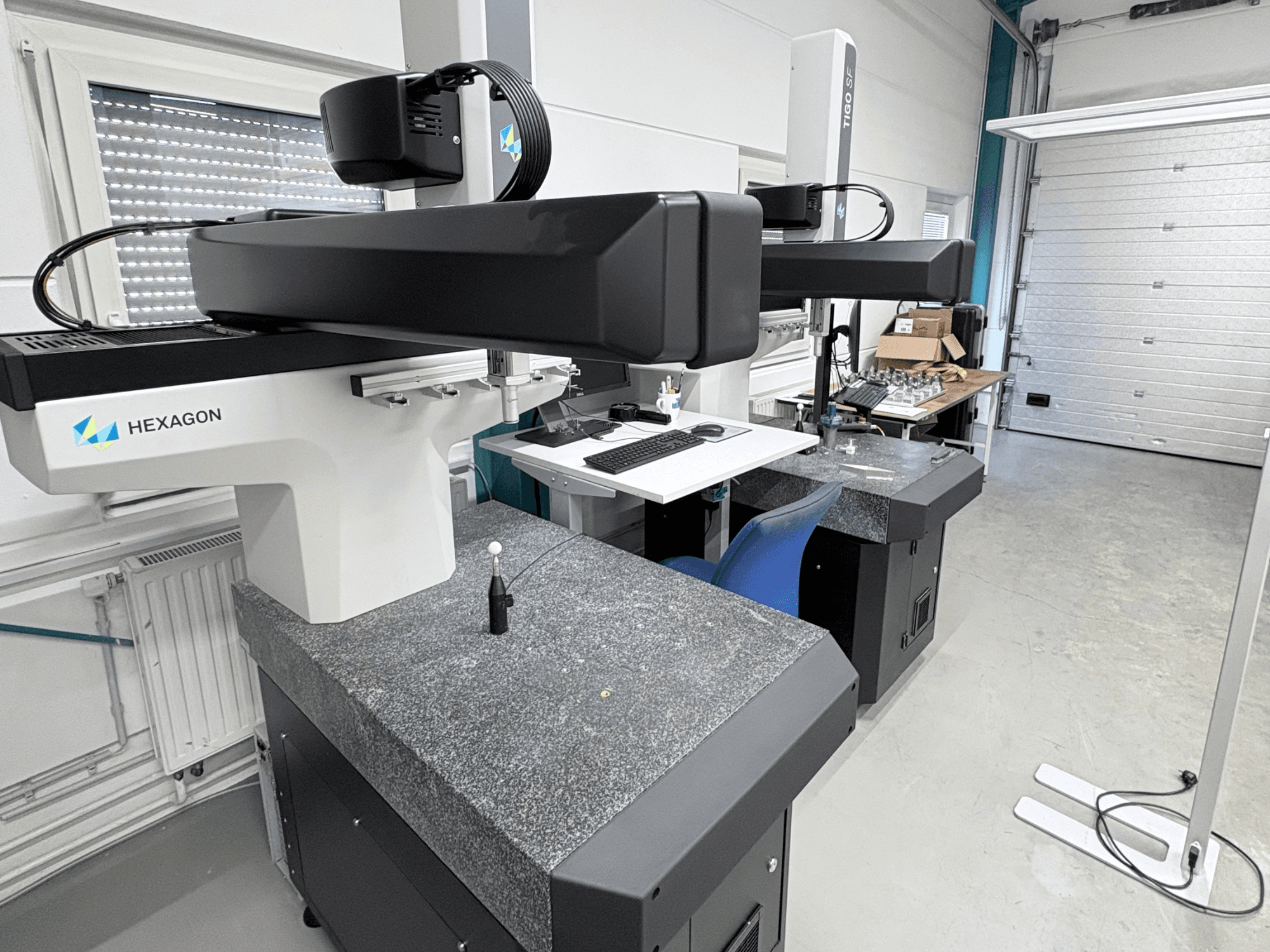 Máquina de medición por coordenadas (CMM) Hexagon Tigo SF en el taller, equipada con una base de granito, una sonda de medición y una estación de trabajo cercana con herramientas.