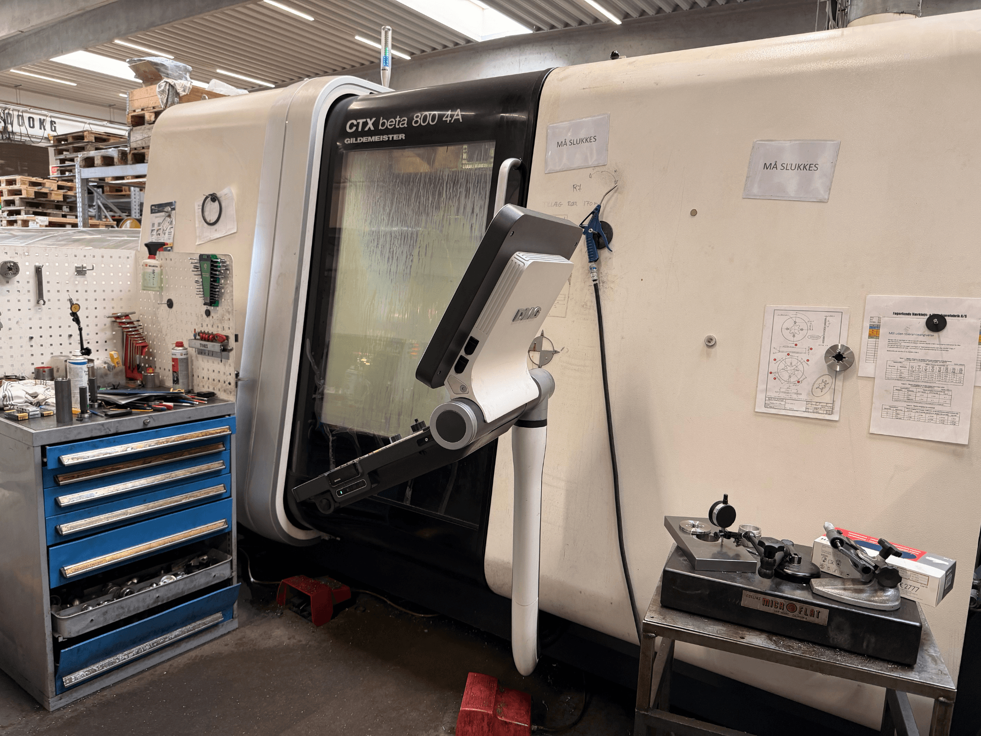 Máquina de torneado vertical DMG MORI CTX Beta 800 4a en un taller, con un brazo de control y documentos técnicos cerca.