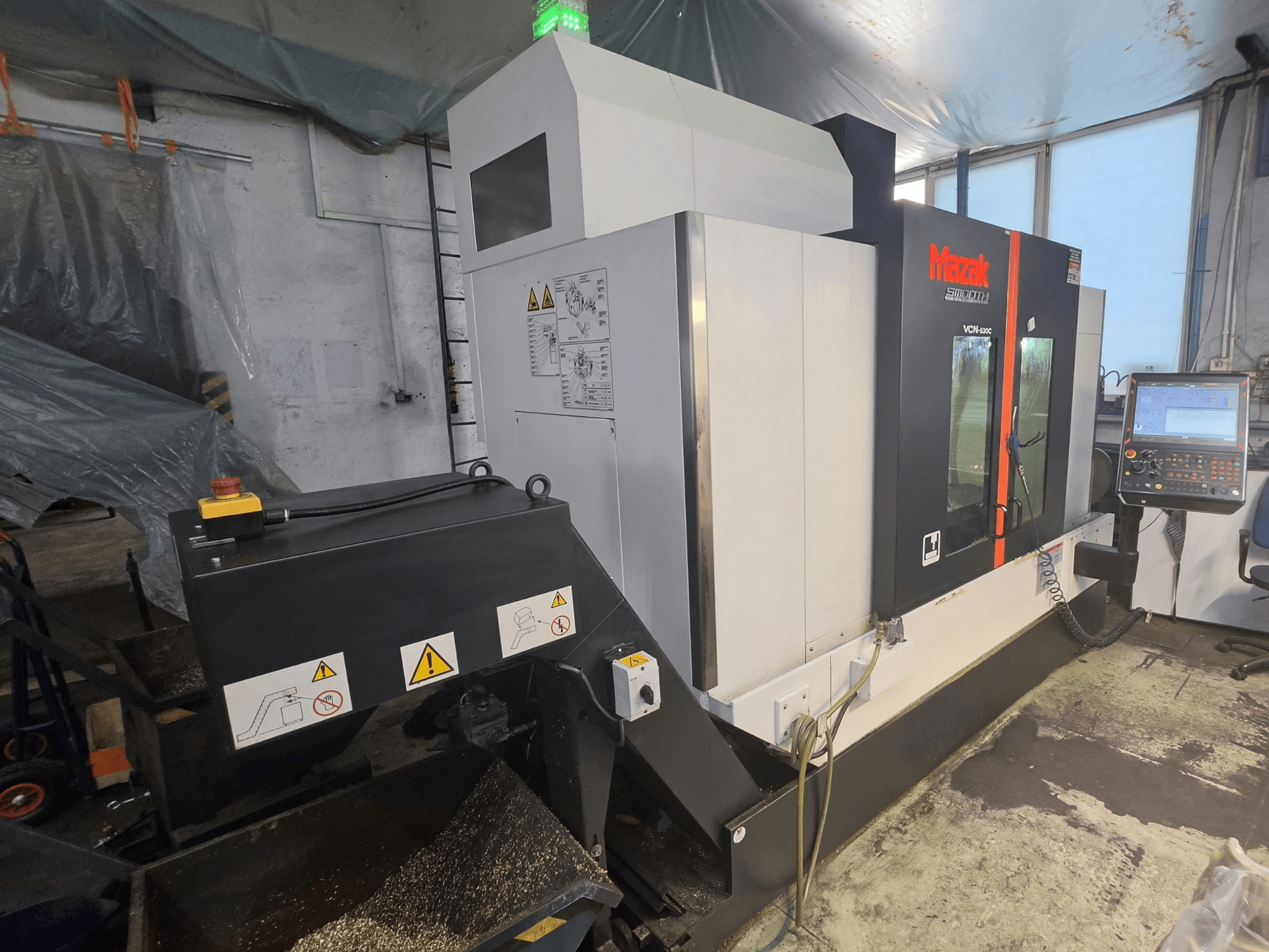 Vista frontal del centro de mecanizado vertical Mazak VCN-530C, en la que se aprecian el panel de control, la cadena de herramientas y los indicadores de funcionamiento.