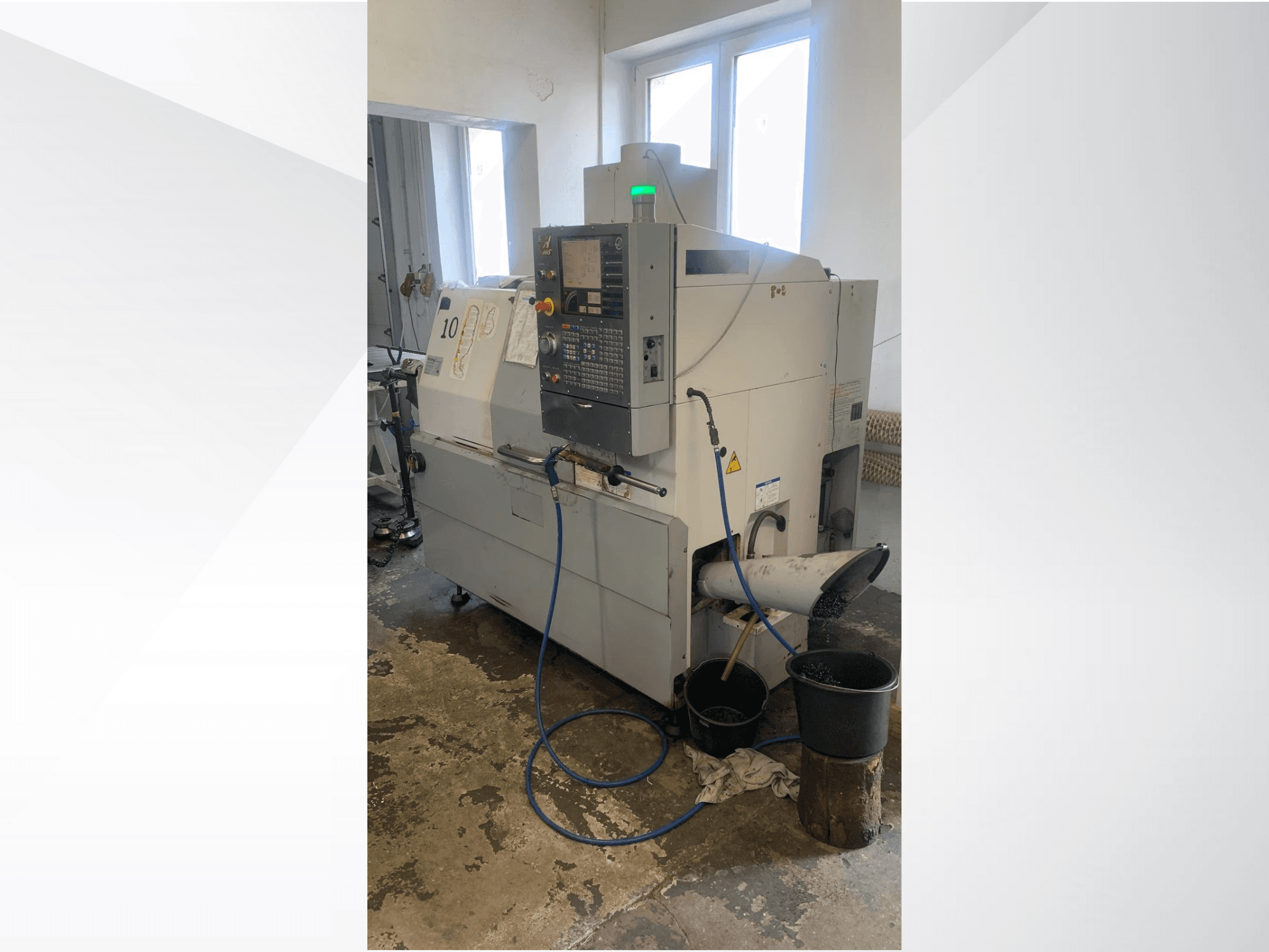 Modelo de máquina CNC Haas con panel de control, vista lateral, con conducto de refrigerante, vertedero de residuos y recipientes de almacenamiento debajo.