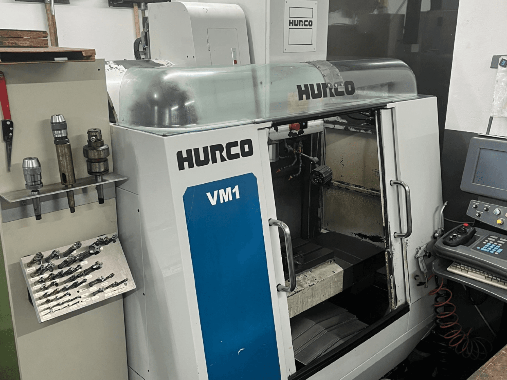 Vista frontal del centro de mecanizado vertical Hurco VM1, con cubierta transparente, panel de control y herramientas montadas.