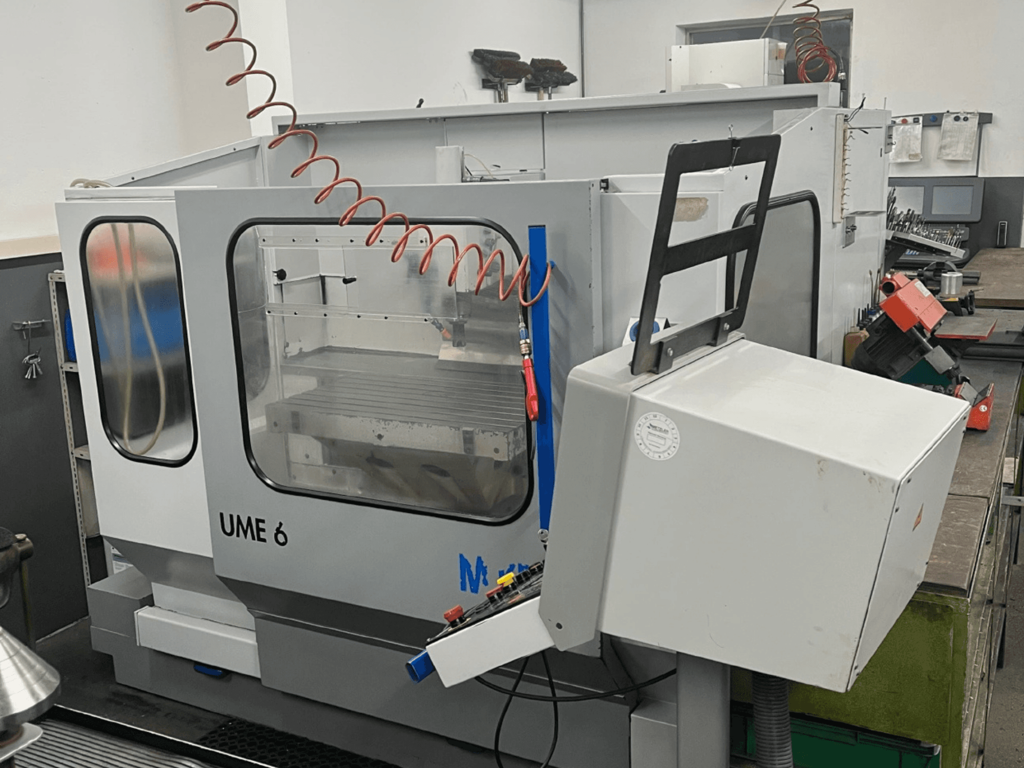 Centro de mecanizado universal MIKRON UME600 en un taller, vista lateral que muestra el panel de control y la caja de protección.