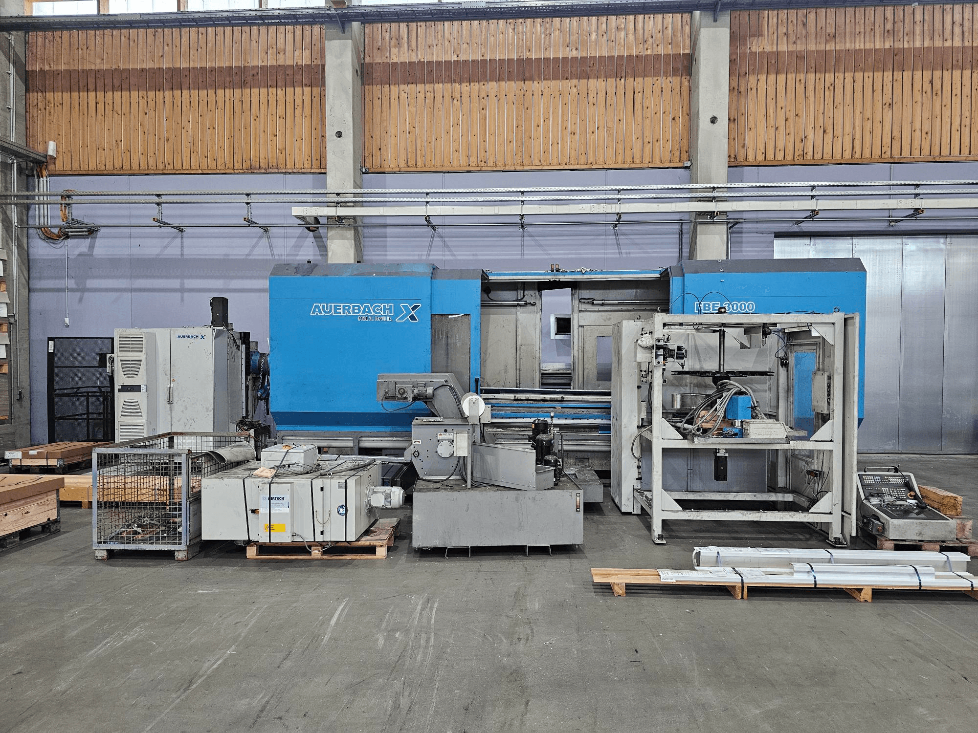 Máquina Auerbach X LBF-3000 en un entorno de fábrica, vista lateral, con componentes grises y azules y panel de control visible.