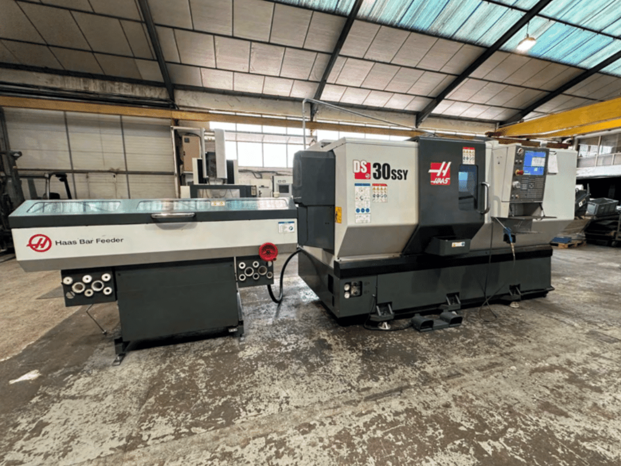 Torno CNC Haas DS-30SSY con alimentador de barras Haas, vista lateral que muestra el panel de control y el mecanismo de alimentación en un taller.