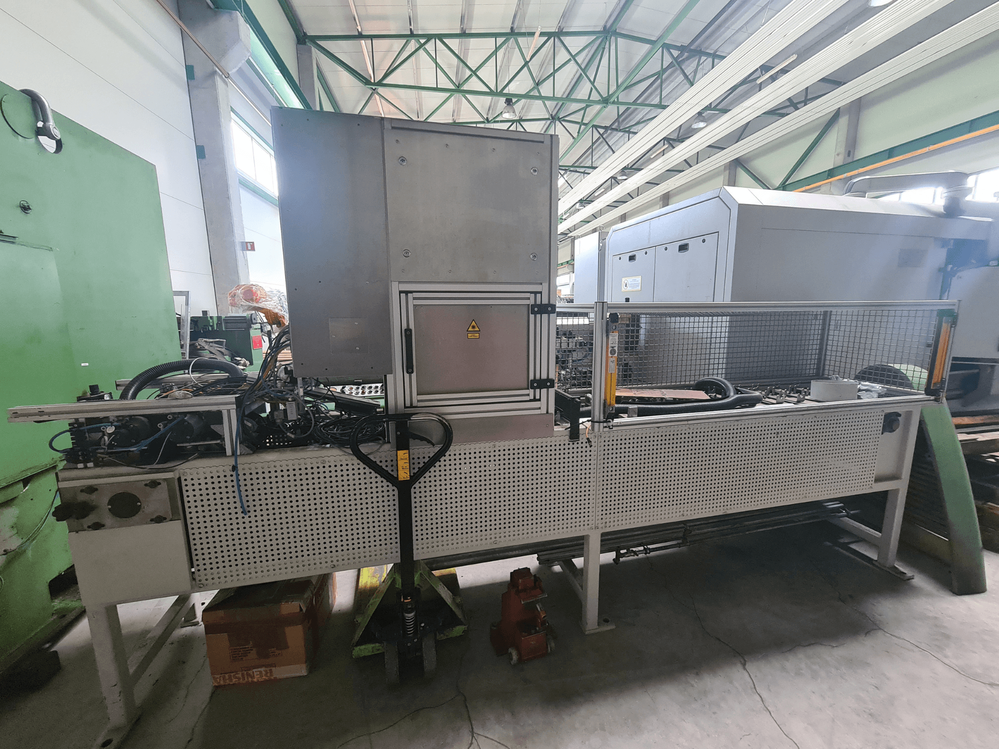 Maquinaria industrial con bastidor metálico, mangueras y panel de control, vista de lado en una fábrica.