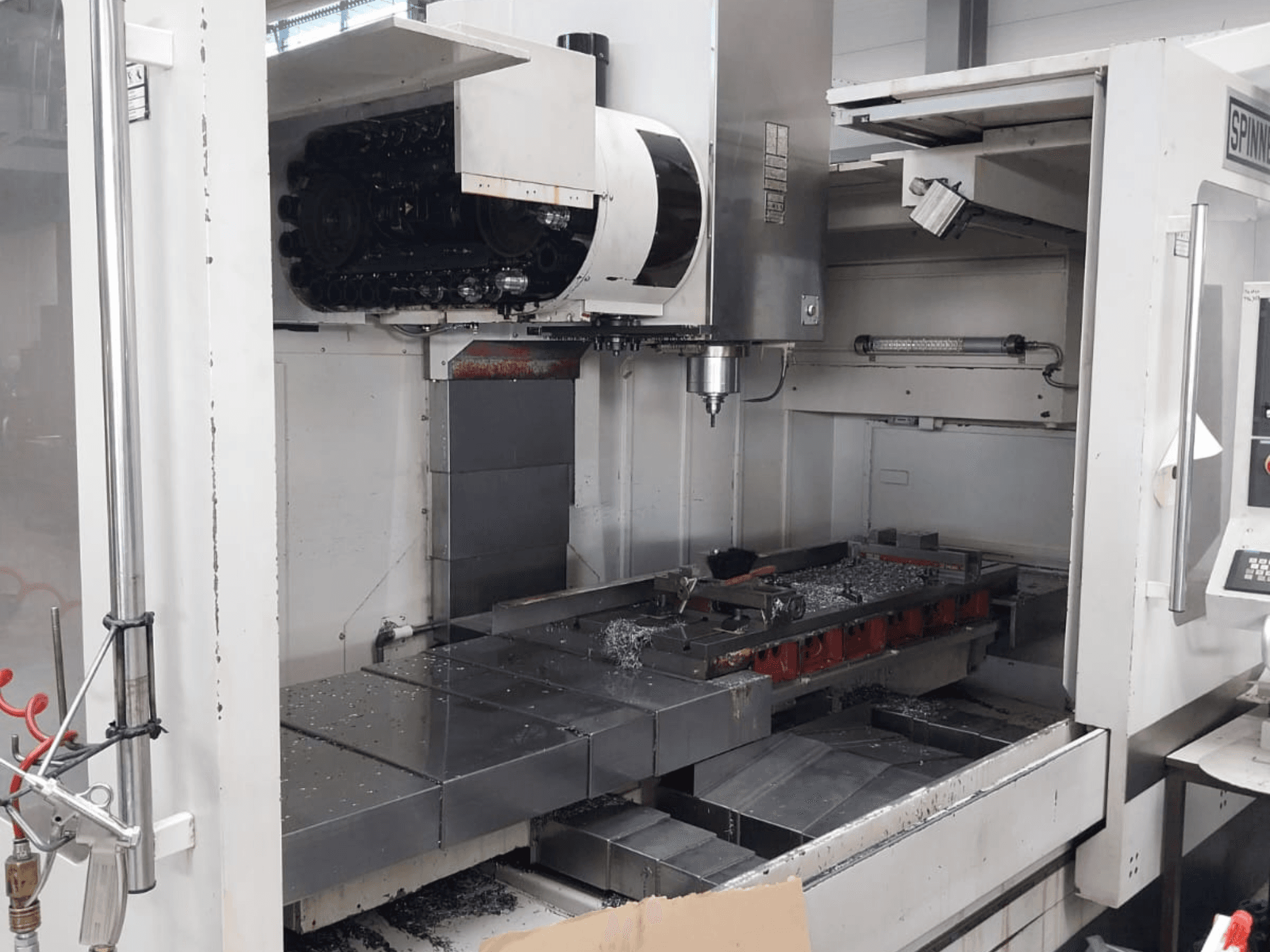Vista frontal del centro de mecanizado vertical SPINNER MVC 1600 que muestra el espacio de trabajo abierto, el husillo y las virutas de metal sobre la mesa.