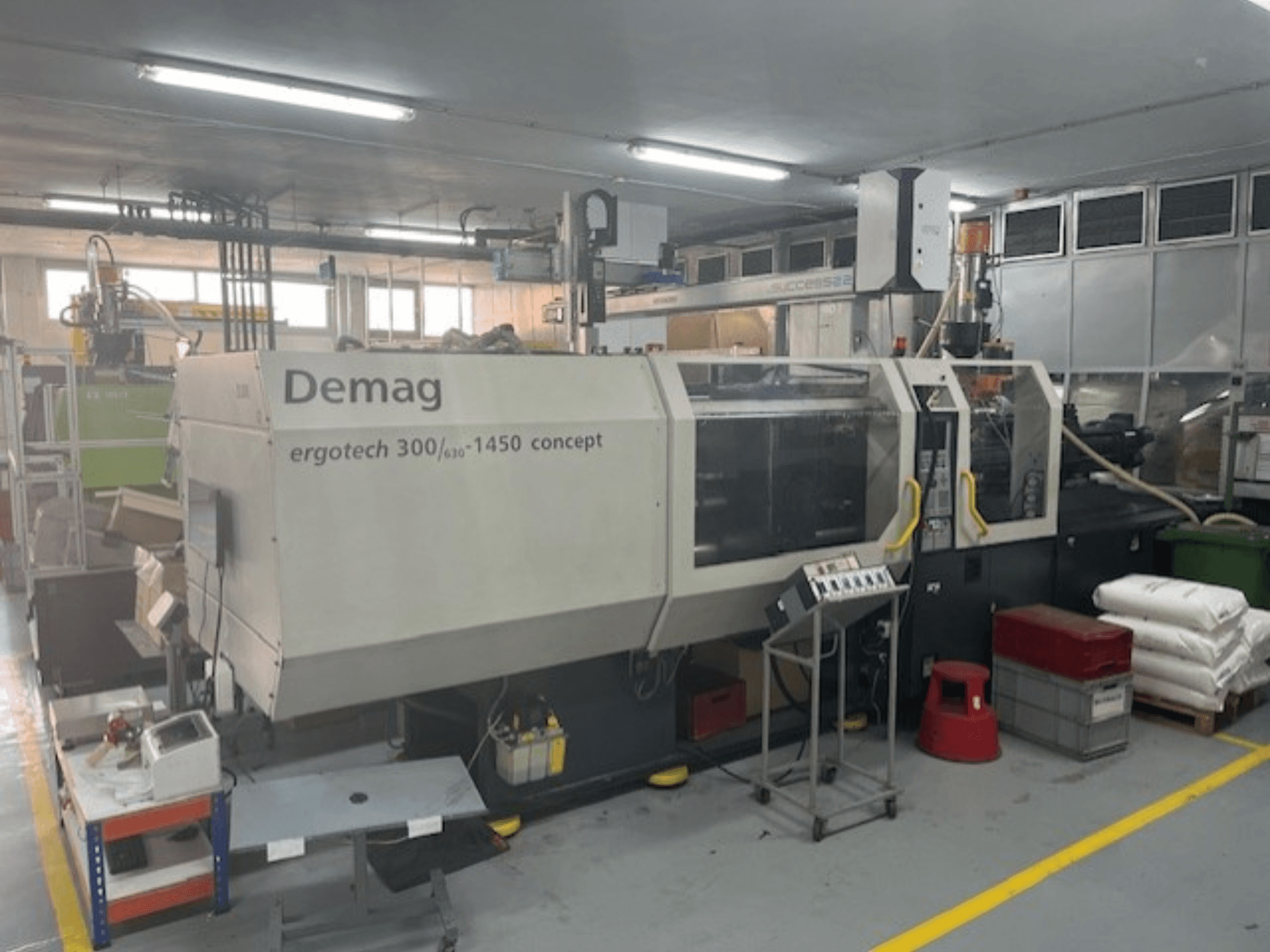 Máquina de moldeo por inyección hidráulica Demag ERGOTECH CONCEPT 3000-1450, vista frontal, con controles operativos y materiales cercanos.