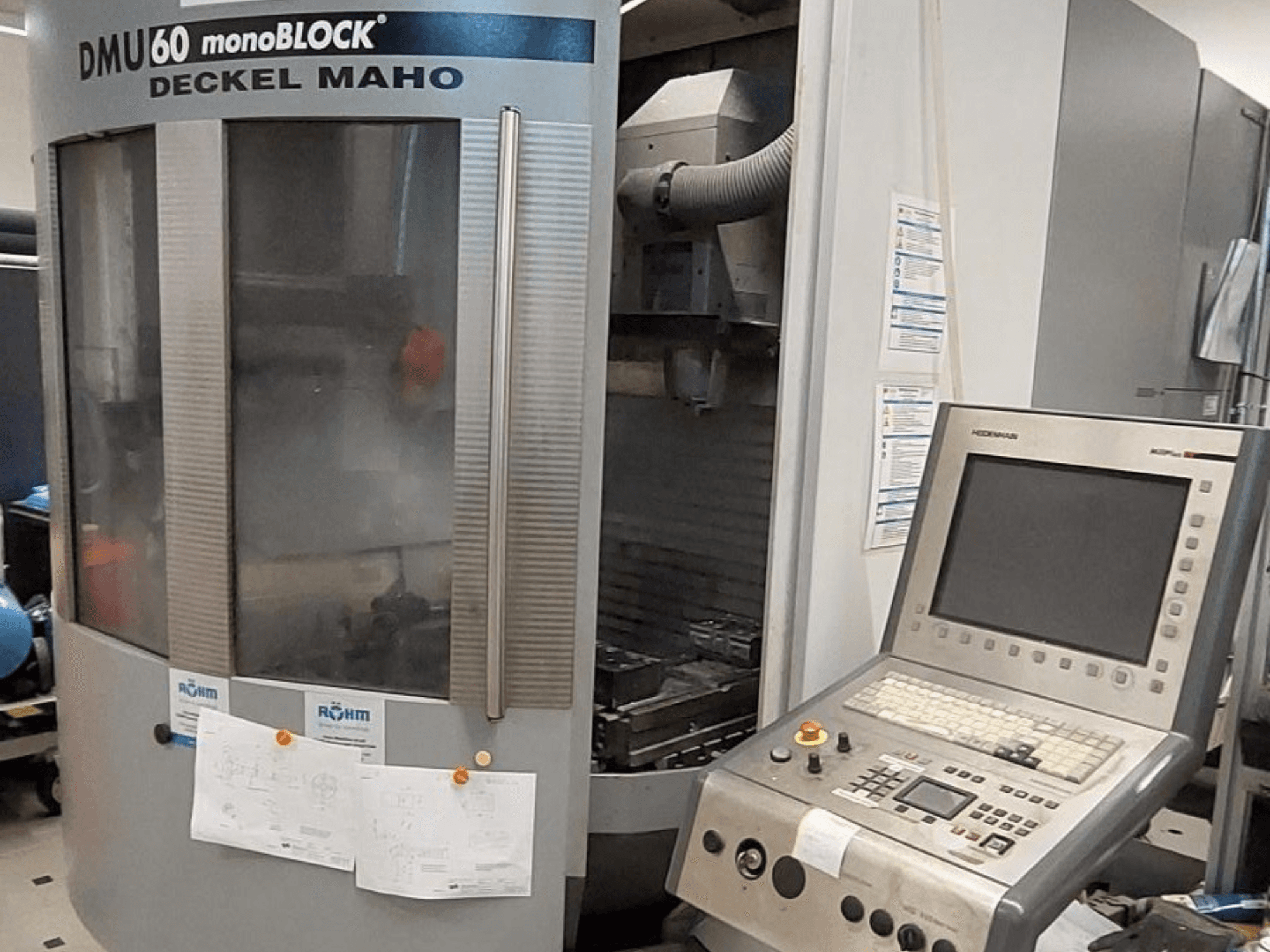 DMU 60 monoBLOCK de Deckel Maho, vista frontal de una fresadora CNC con panel de control y planos técnicos adjuntos.