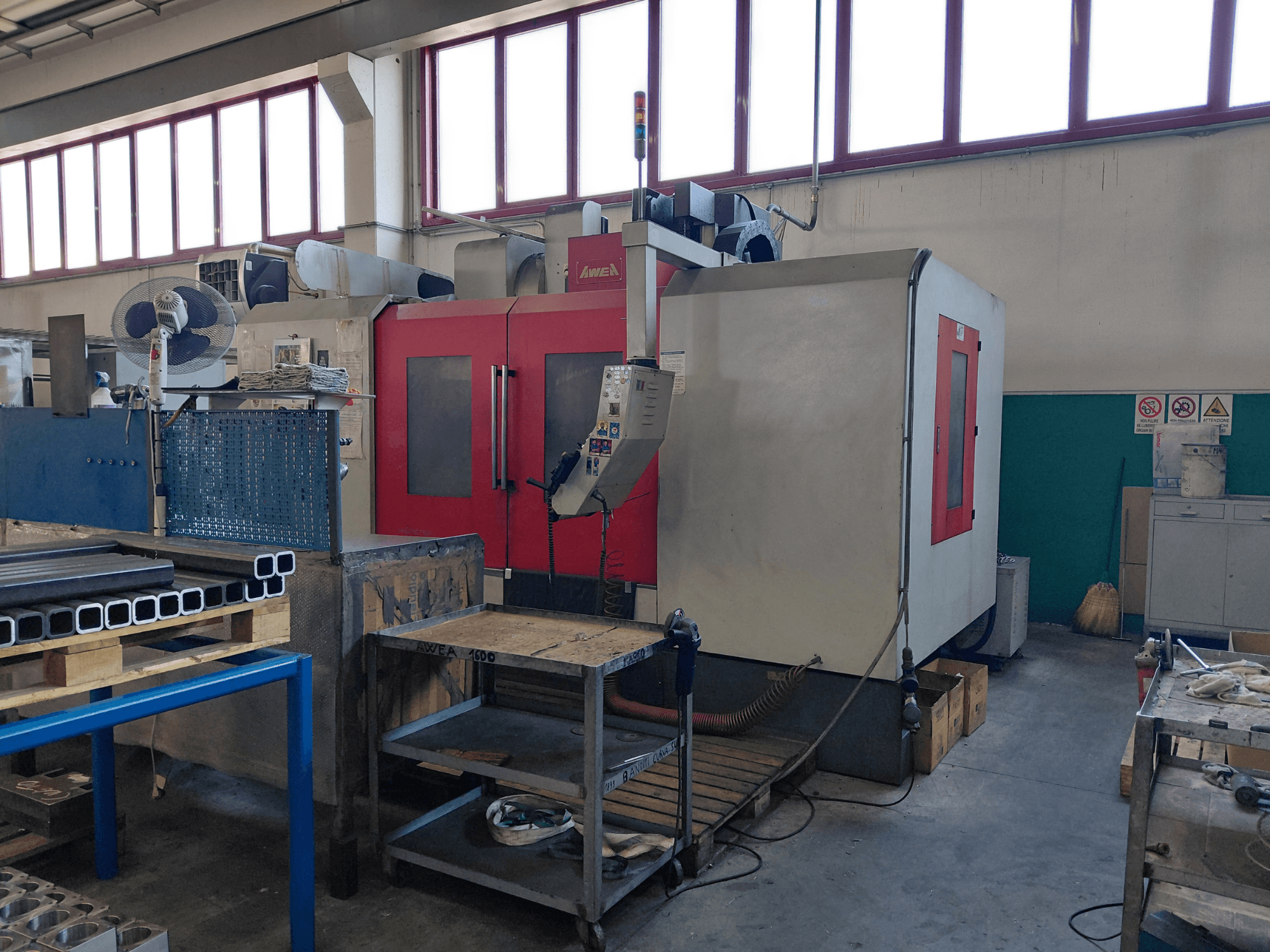 Centro de mecanizado vertical AWEA BM-1600, vista frontal, con la estructura en rojo y gris; se aprecian cerca el banco de trabajo y las herramientas.