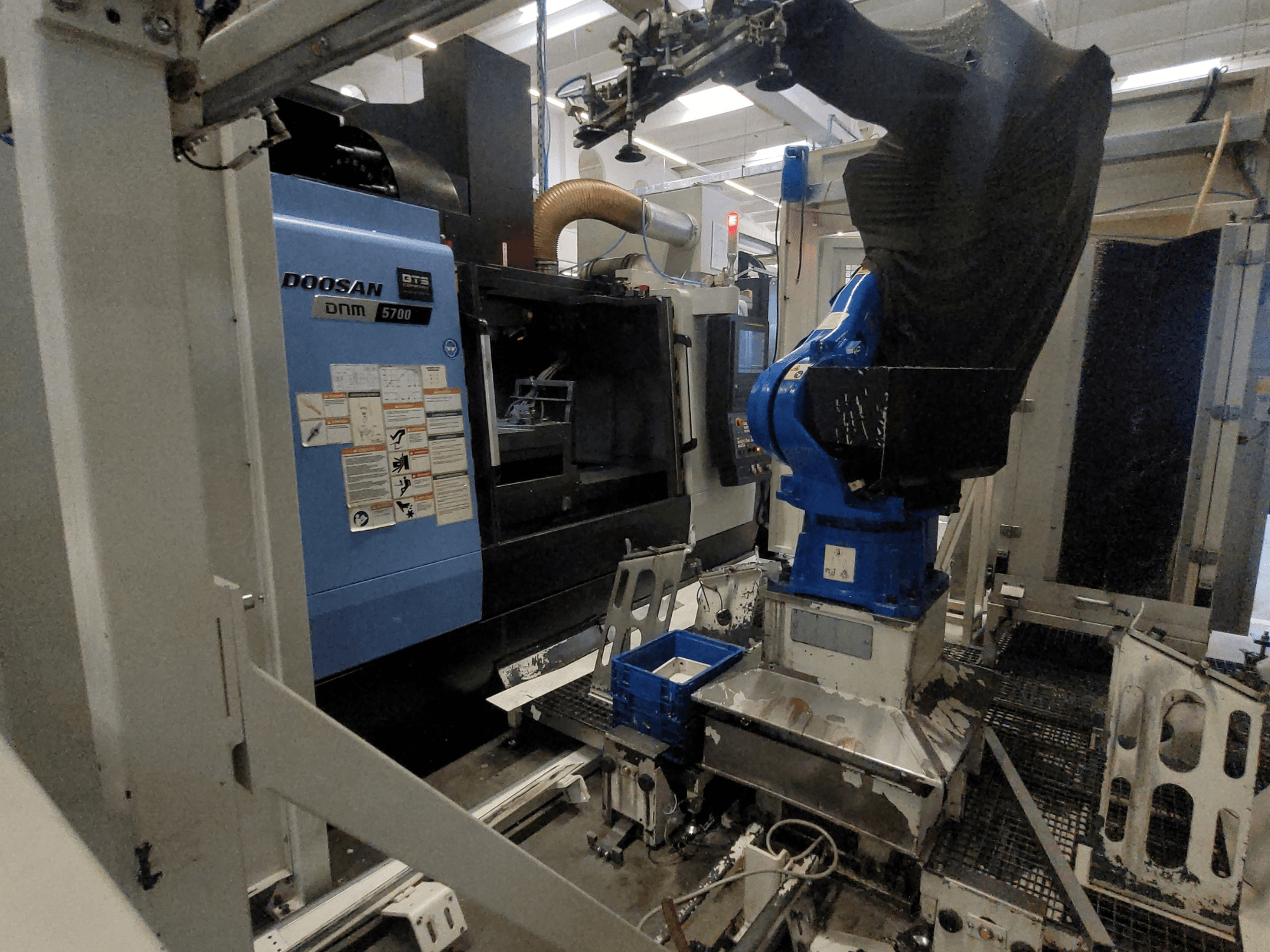 Centro de mecanizado vertical DOOSAN DNM 5700 en un entorno industrial, en el que se aprecia su vista frontal y la integración del brazo robótico.