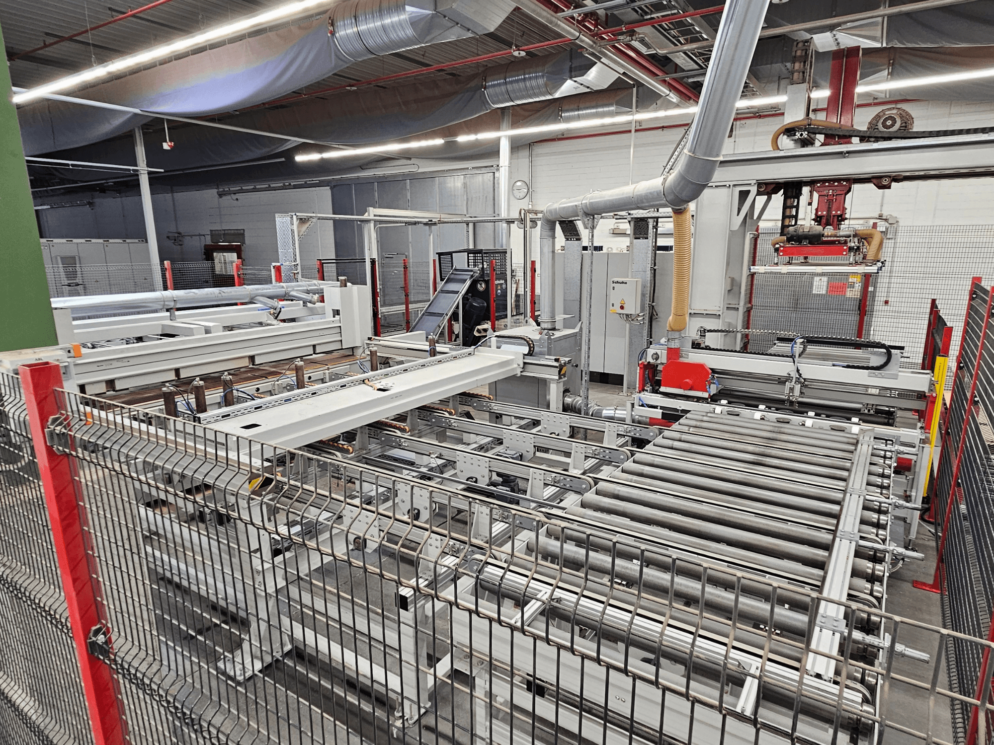 Sierra de paneles HOLZMA HPP81-3200 mostrada en una vista frontal, con rodillos transportadores y componentes de maquinaria en un entorno de taller.