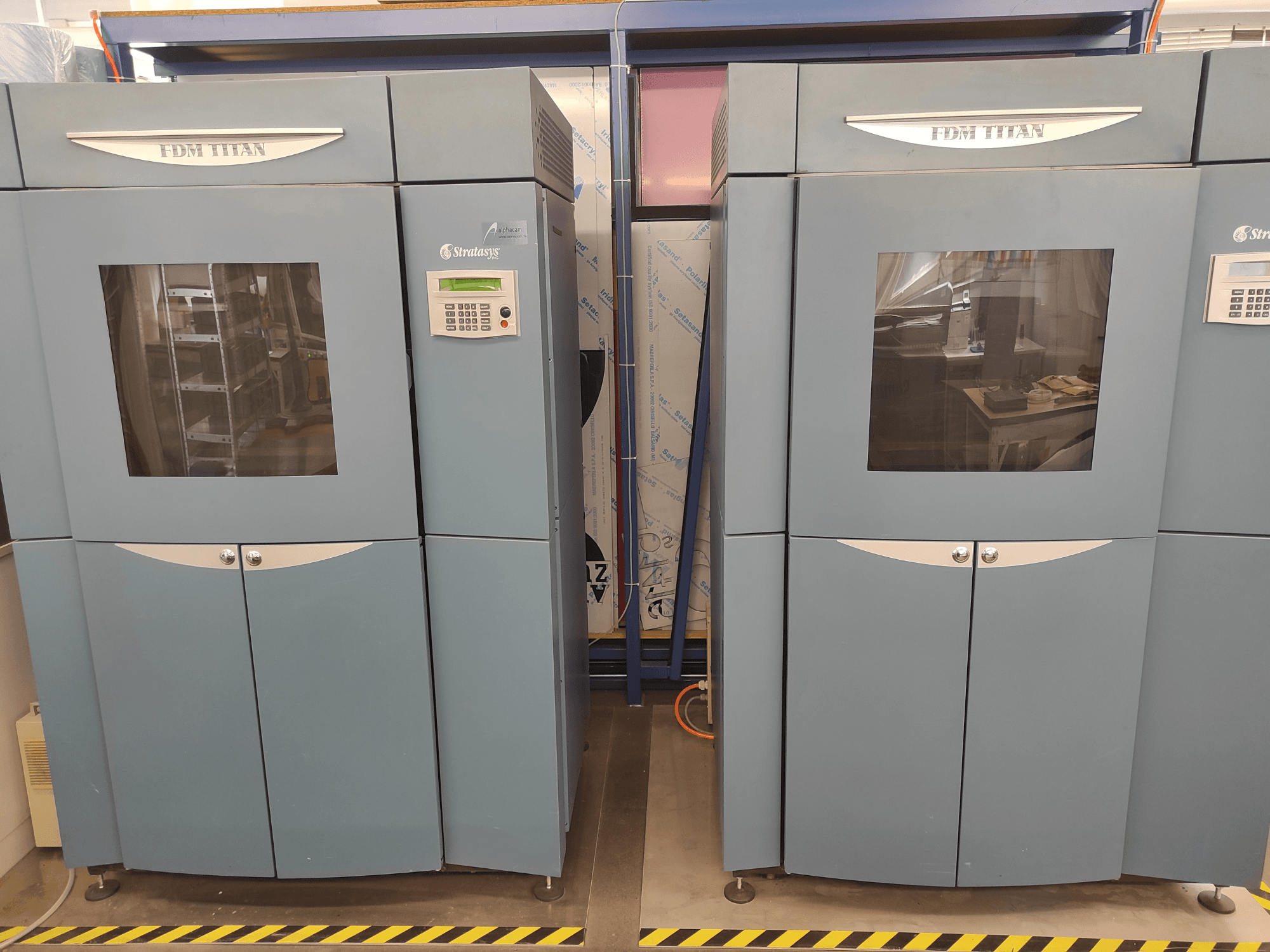 Impresora 3D FDM TitanTI de Stratasys, vista frontal, con dos puertas y panel de control, situada en un entorno industrial.