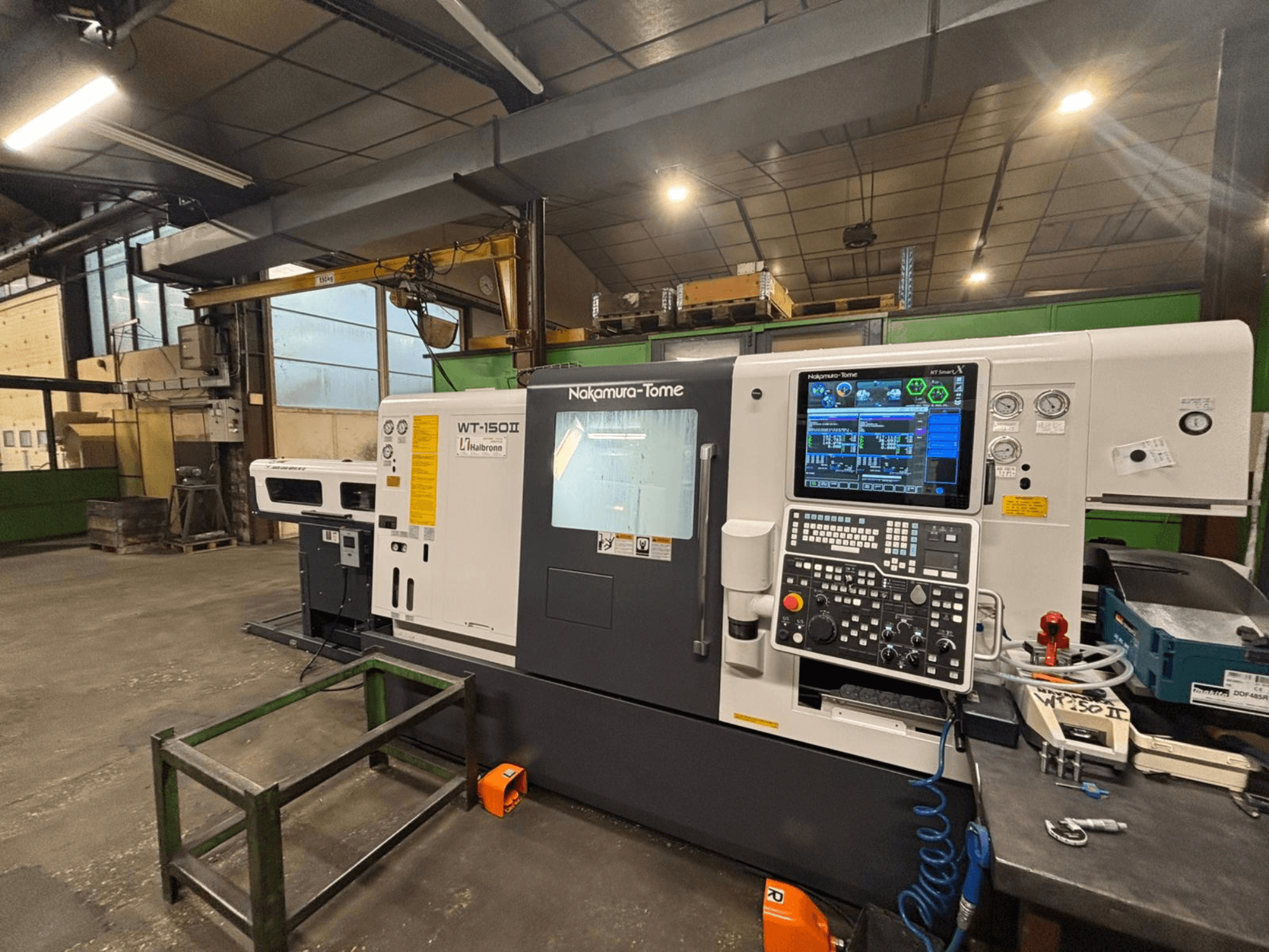 Máquina Nakamura-Tome WT-150II, vista frontal, con panel de control y herramientas visibles en un banco de trabajo en un taller.