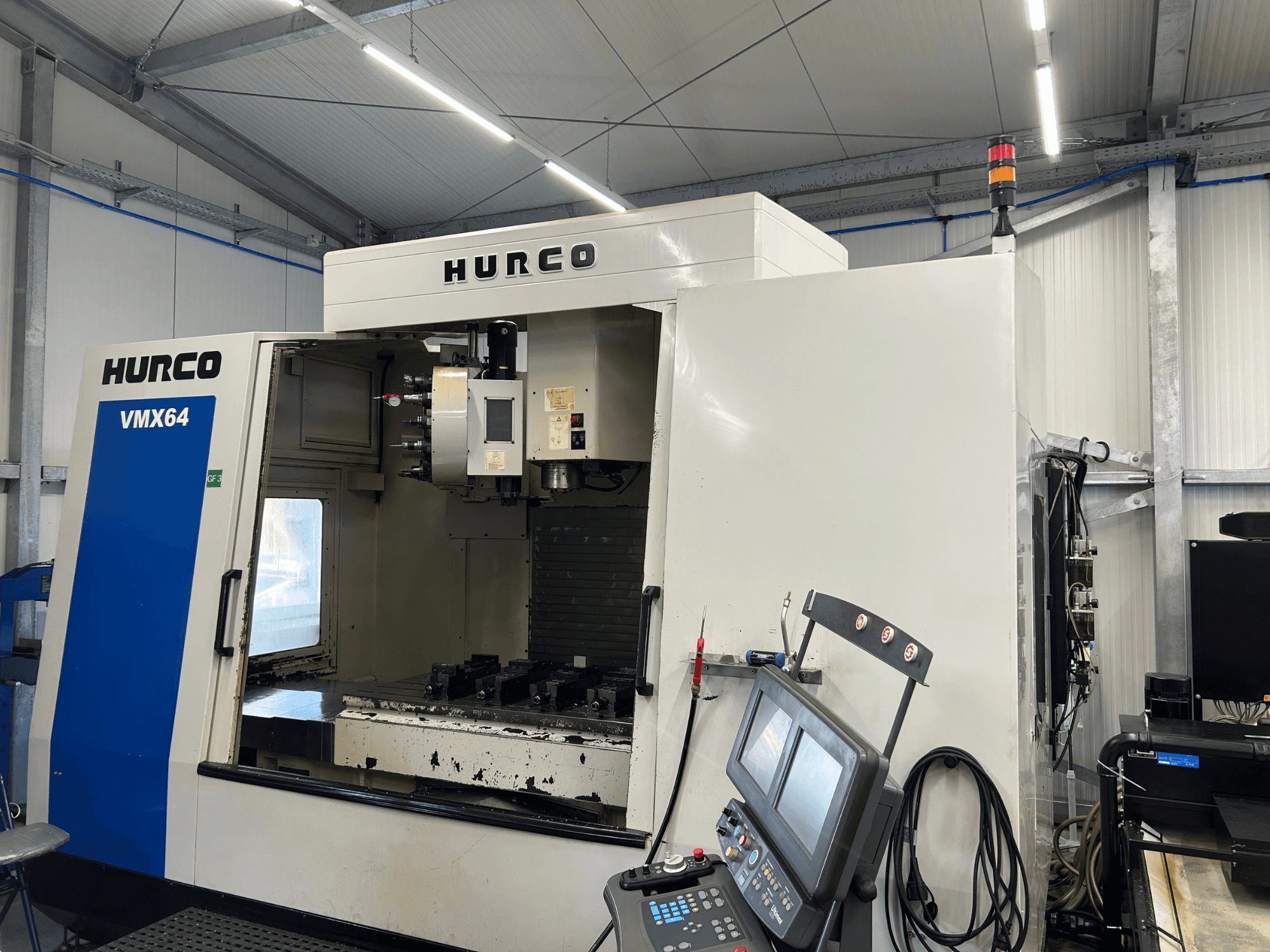 Centro de mecanizado vertical Hurco VMX 64, vista frontal, en la que se aprecian el panel de control y el espacio de trabajo abierto con las herramientas.