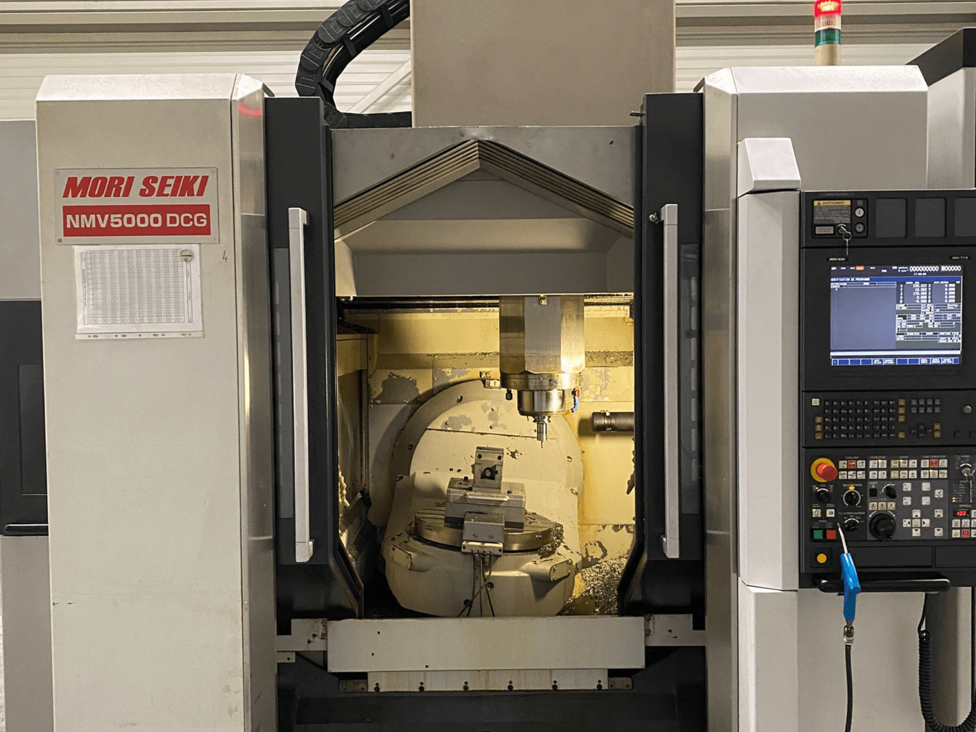 Centro de mecanizado universal MORI SEIKI NMV 5000DCG, vista frontal mostrando el panel de control y el área de mecanizado interior.