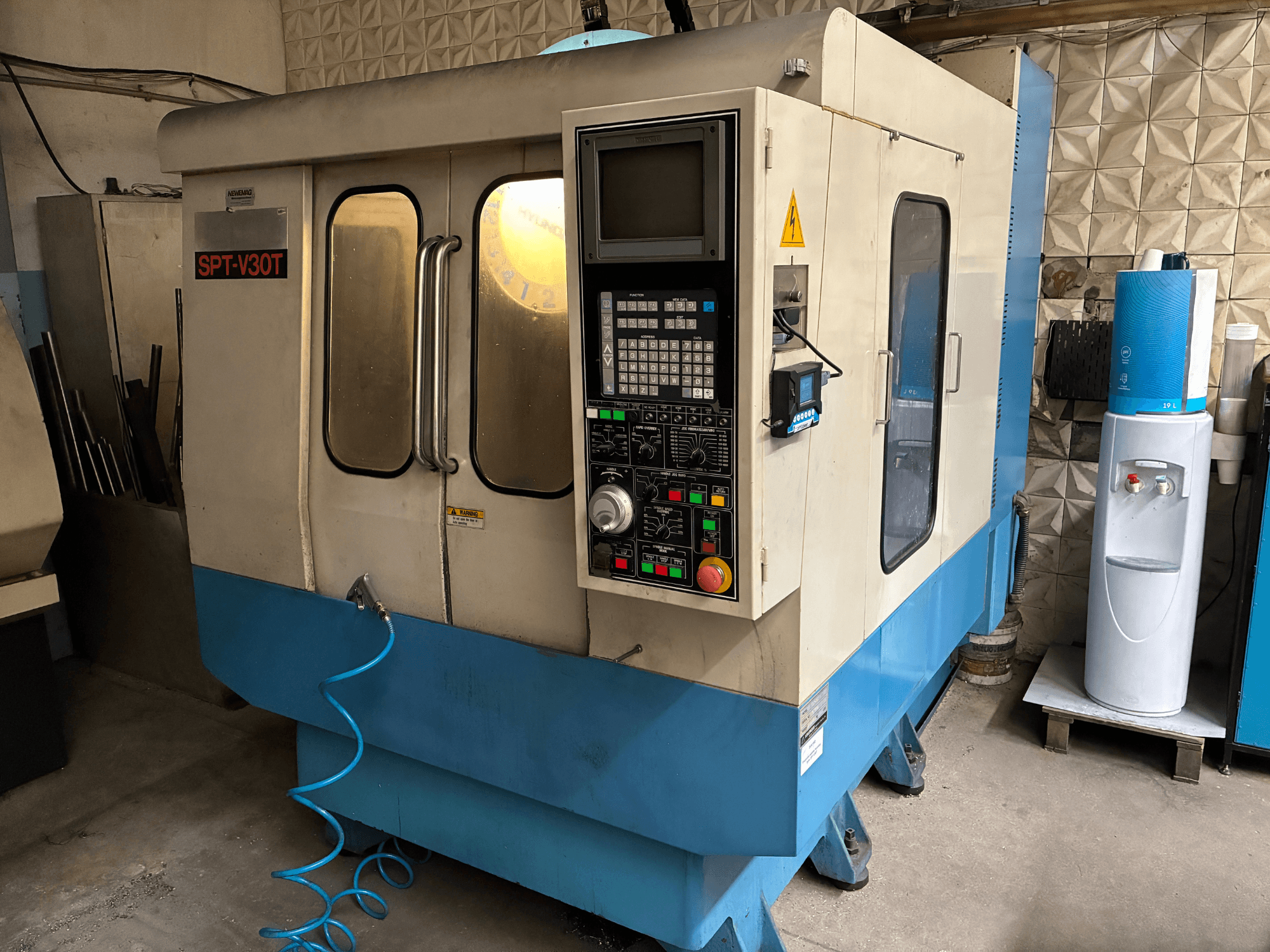 Máquina CNC SPT-V30T en azul y blanco, vista frontal que muestra el panel de control, las puertas y la manguera de aire. Perfecta para el mecanizado de precisión.