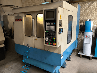 Máquina CNC SPT-V30T en azul y blanco, vista frontal que muestra el panel de control, las puertas y la manguera de aire. Perfecta para el mecanizado de precisión.