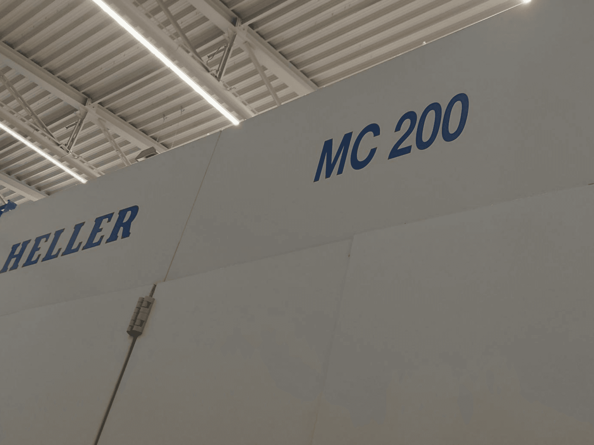 Centro de mecanizado horizontal Heller MC 200, mostrado lateralmente, destacando la marca y el modelo en letras azules sobre una superficie blanca.