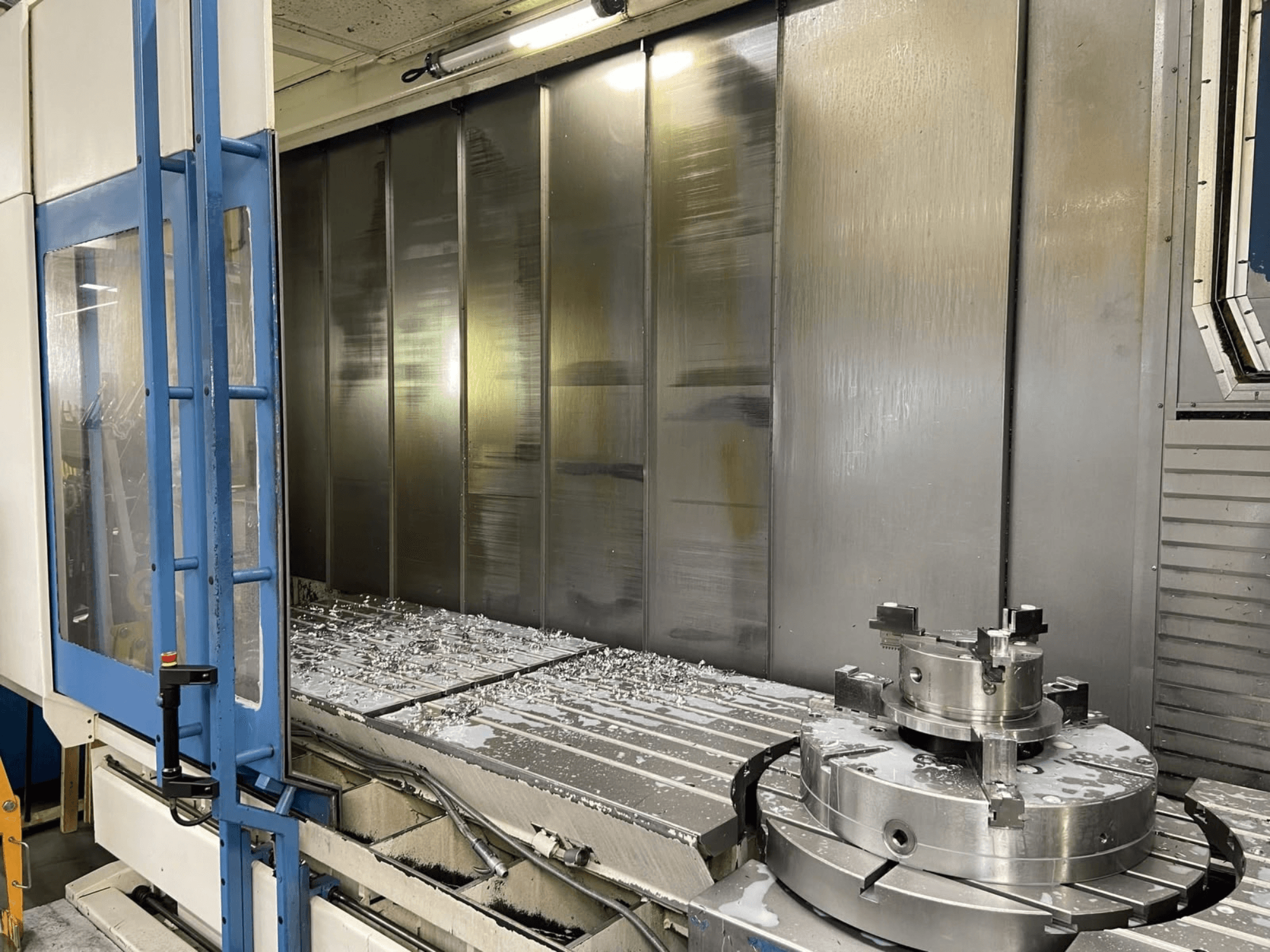 Centro de mecanizado vertical AXA VHC-3-3000-M/E, vista frontal, en la que se aprecian las virutas de metal fresadas sobre la mesa de trabajo y las herramientas de corte.