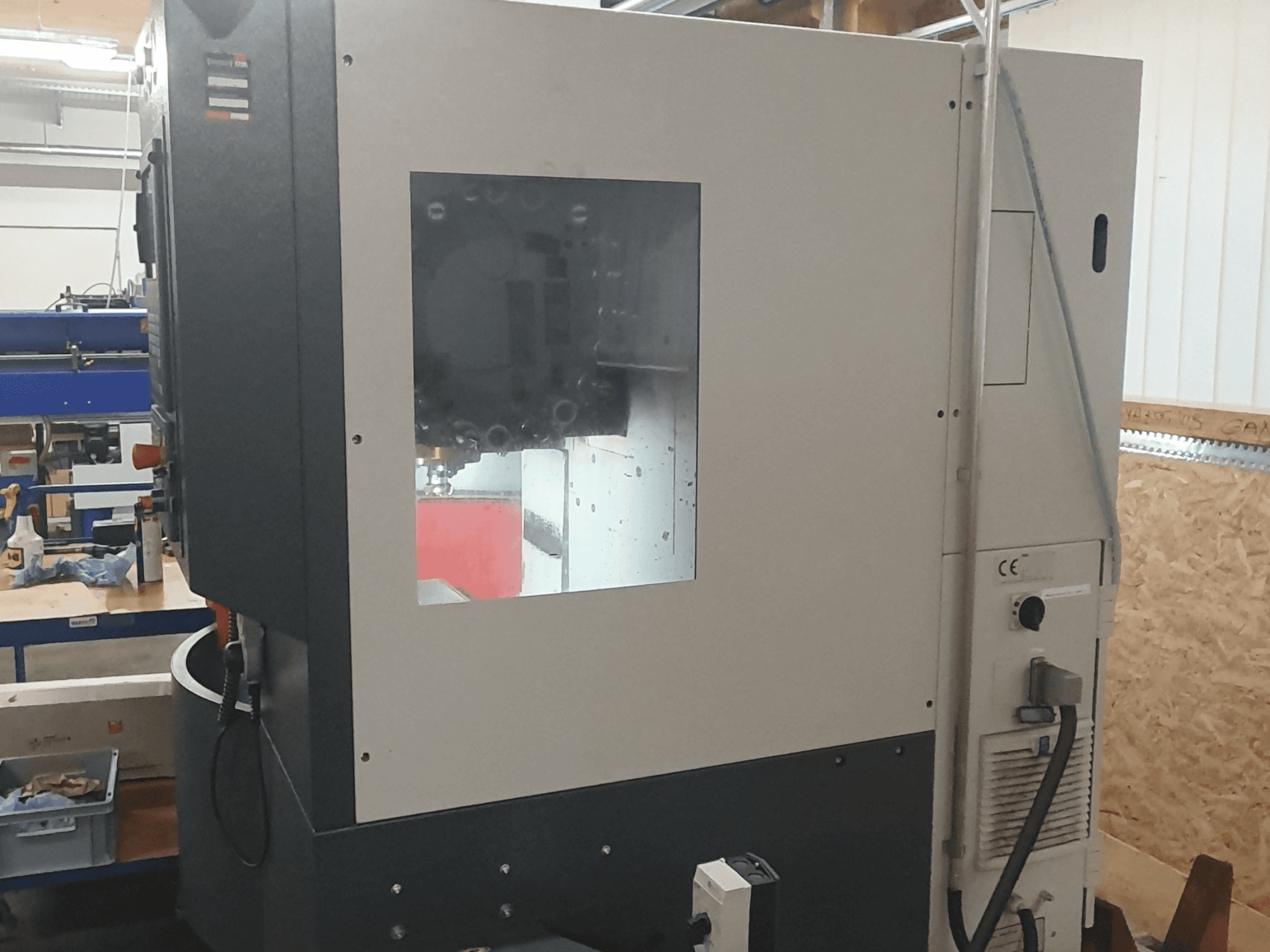 Vista lateral de una máquina para trabajar el metal con panel de control visible, gran ventana de visualización e intrincados componentes internos.