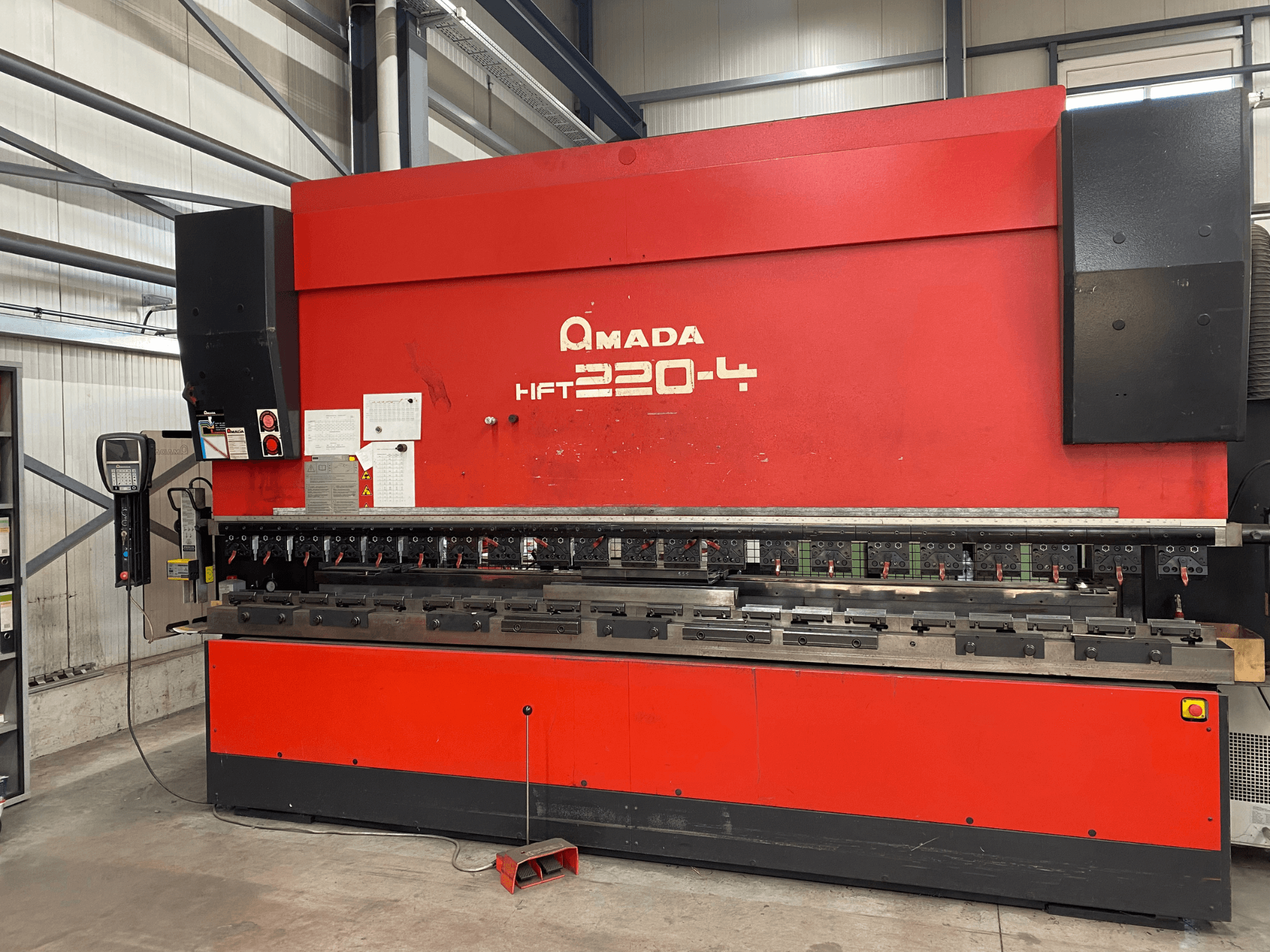 Plegadora AMADA HFT 220-4 roja en una configuración de fábrica, vista frontal que muestra el panel de control y las herramientas de plegado en la superficie de trabajo.
