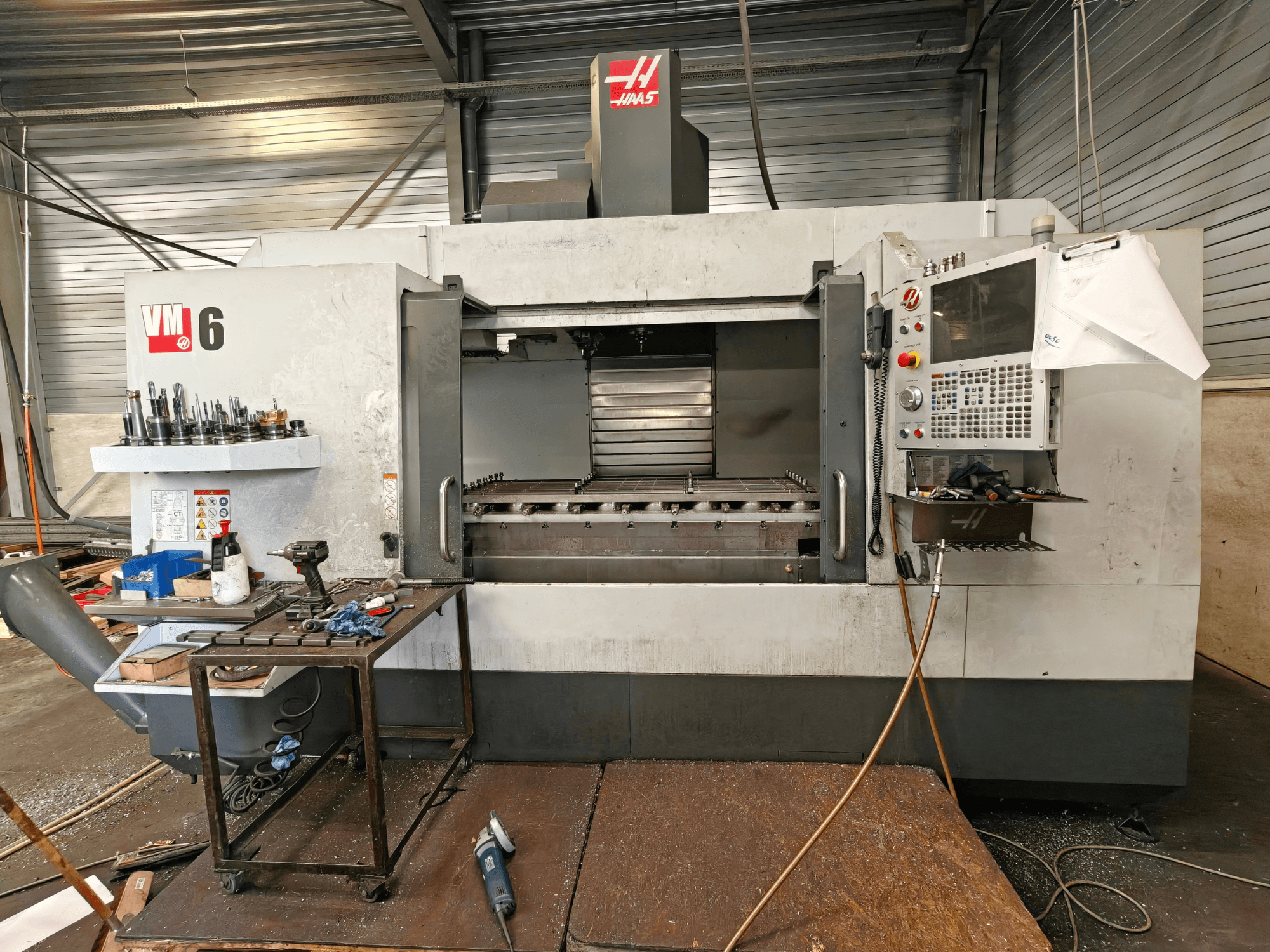 Centro de mecanizado vertical Haas VM-6, vista frontal, en la que se aprecian el almacén de herramientas, el panel de control y los residuos en la zona de trabajo.