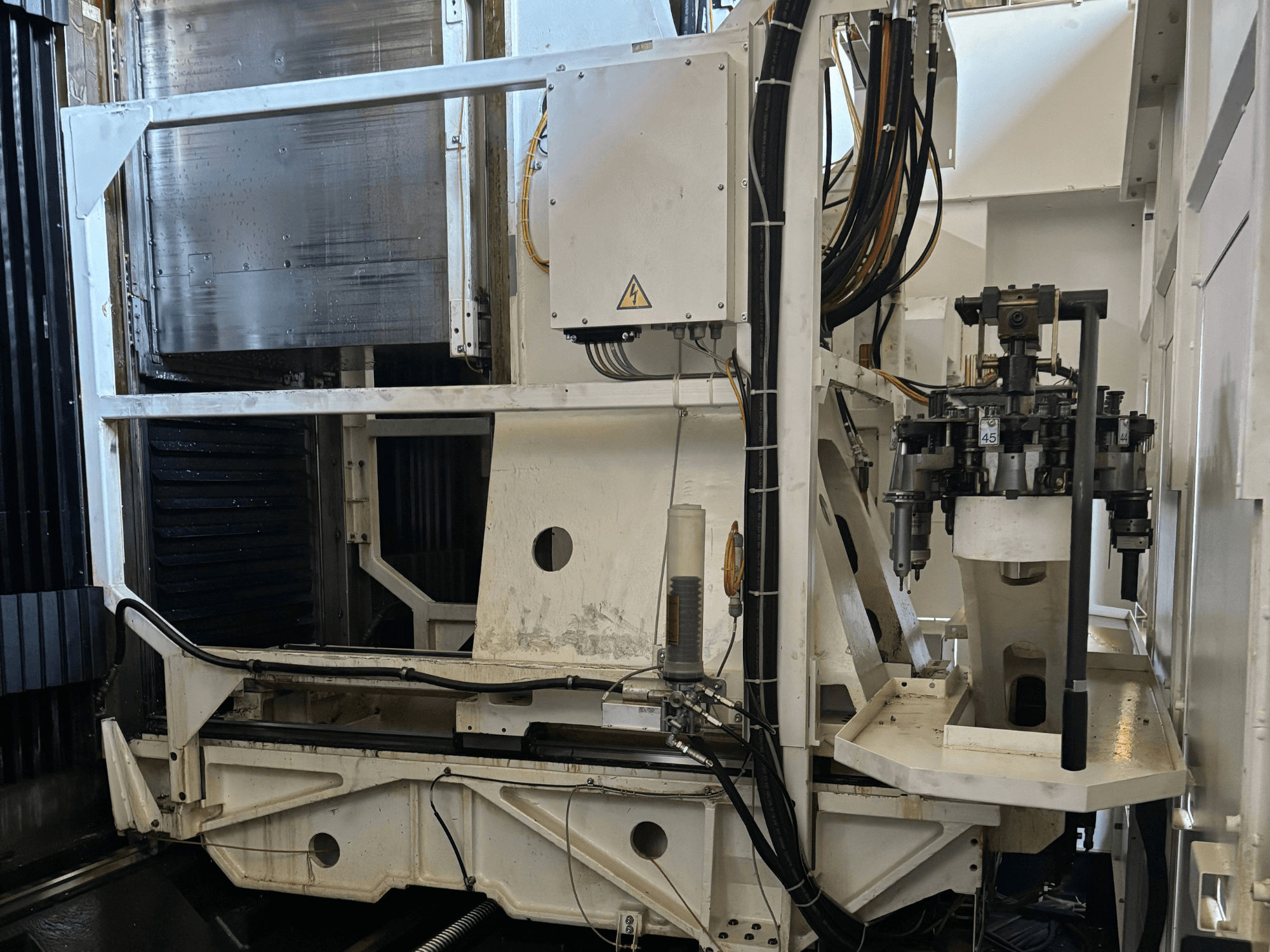 Vista lateral de máquina industrial que muestra una fresadora CNC blanca con herramientas visibles, tuberías y panel de control.