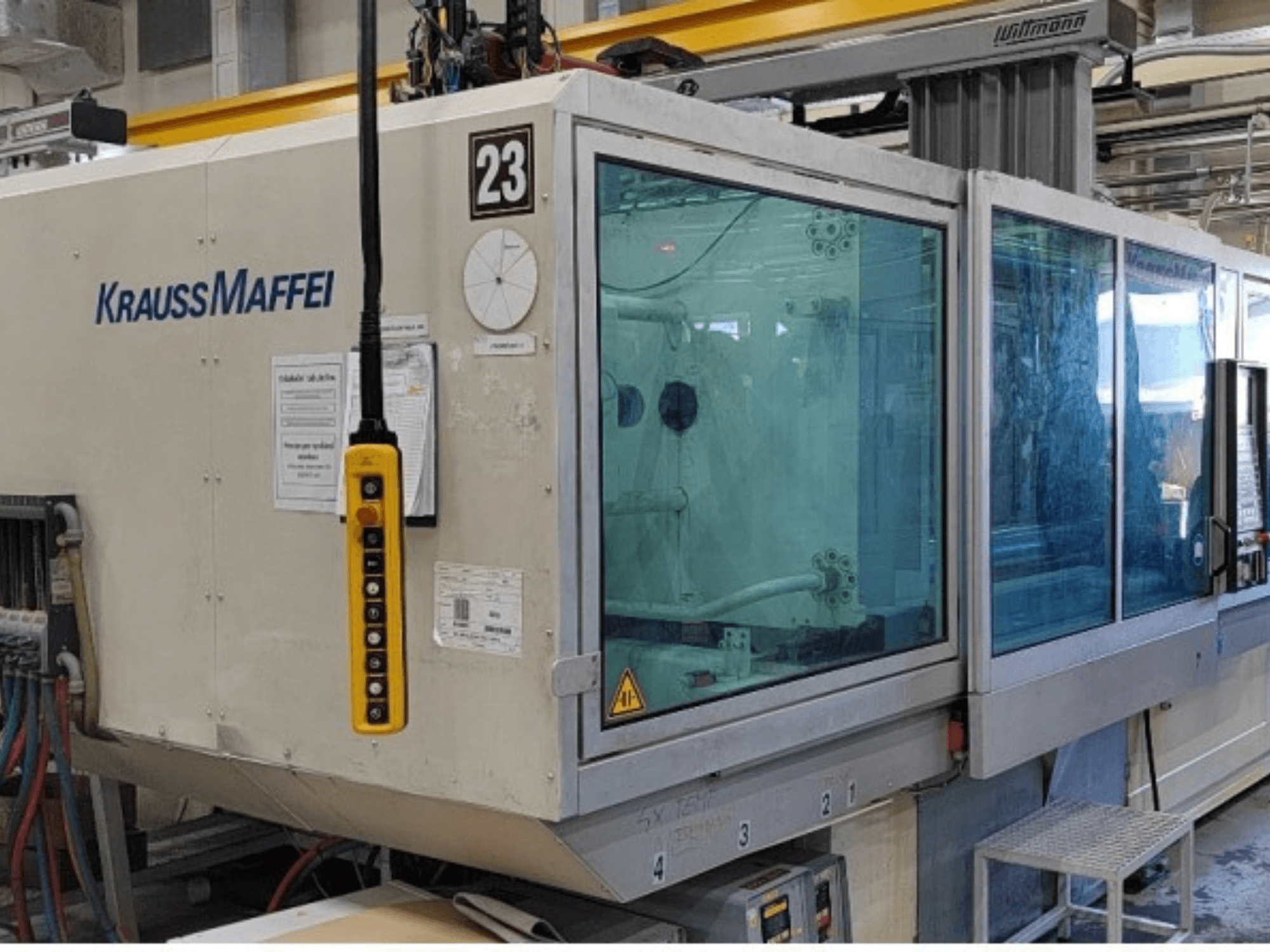 Máquina de moldeo por inyección hidráulica Krauss Maffei KM 350-1900 C2, vista frontal en la que se aprecian el panel de control y la cabina de seguridad transparente.