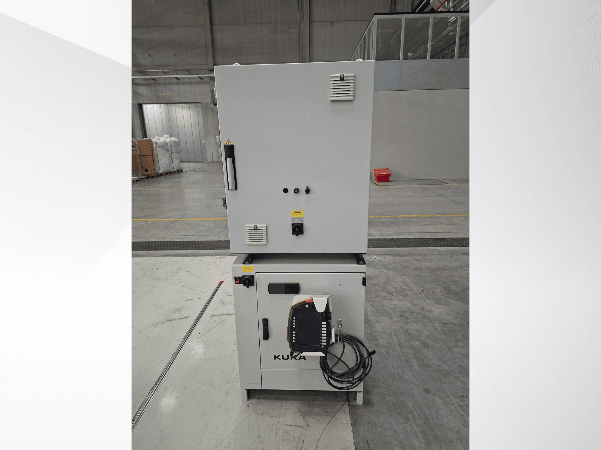Controlador del brazo robótico KUKA KR 90 R2700 PRO C4 FLR, vista frontal en la que se aprecian el panel de control y las etiquetas de seguridad en un amplio almacén.