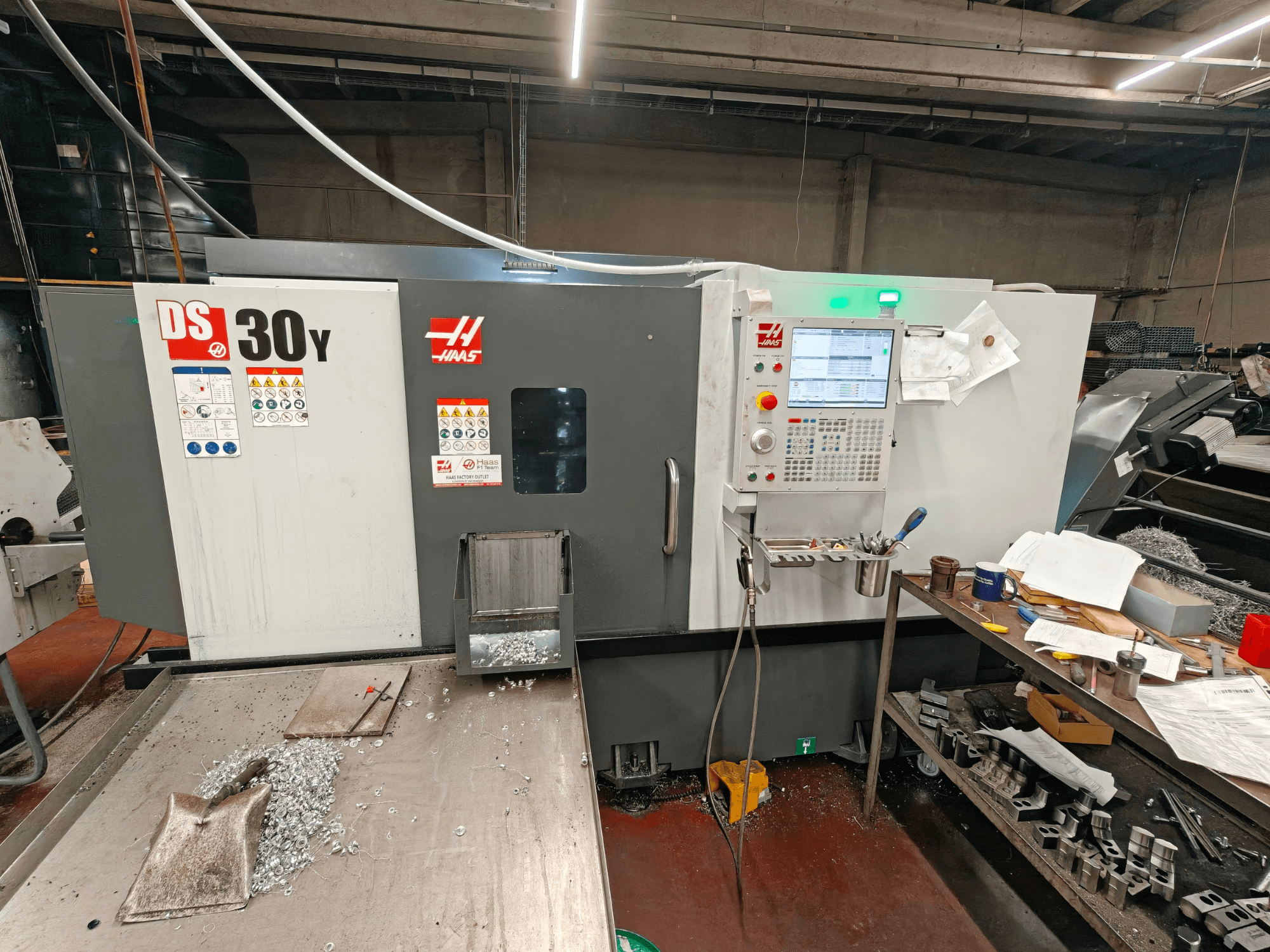 Torno horizontal HAAS DS30Y en un taller; vista frontal en la que se aprecian el panel de control y las virutas de metal sobre la superficie.