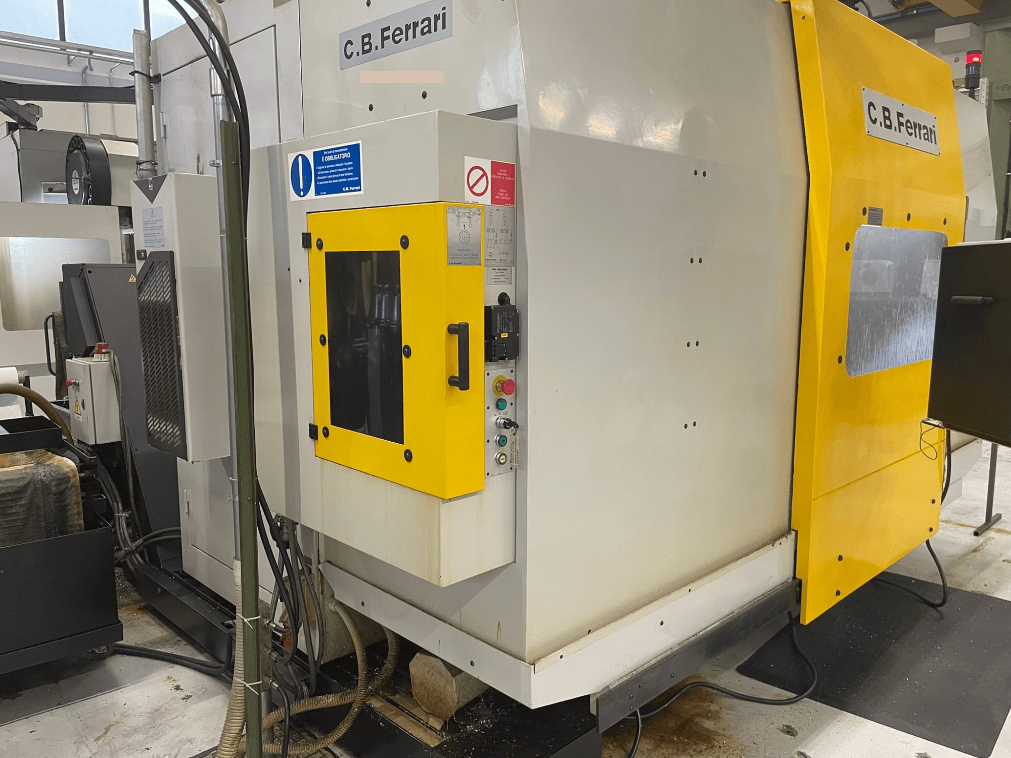 Máquina industrial C.B. Ferrari, vista frontal; presenta puerta amarilla, panel de control y componentes de mecanizado visibles.
